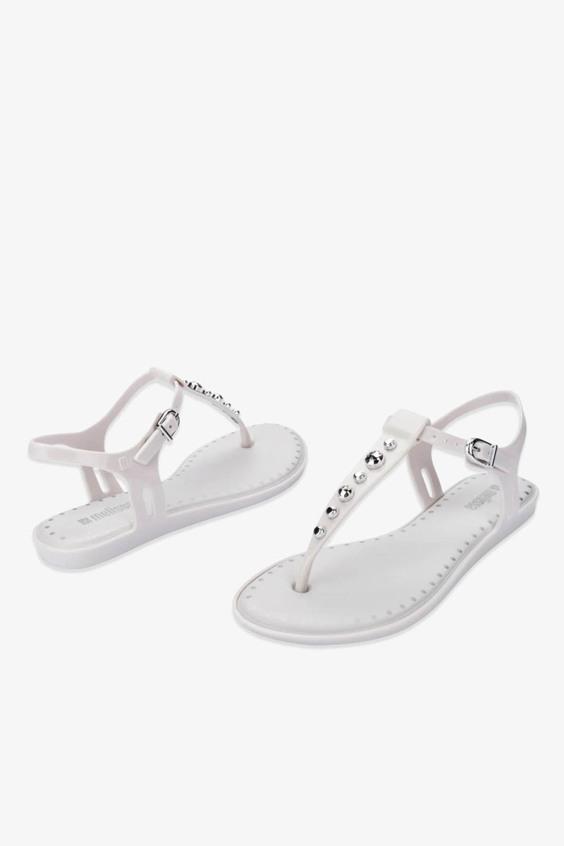 A pair of Solar Boho Thong Sandals in white, featuring ankle straps and silver studs adorning the top, displayed from both side and front angles against a plain white background.