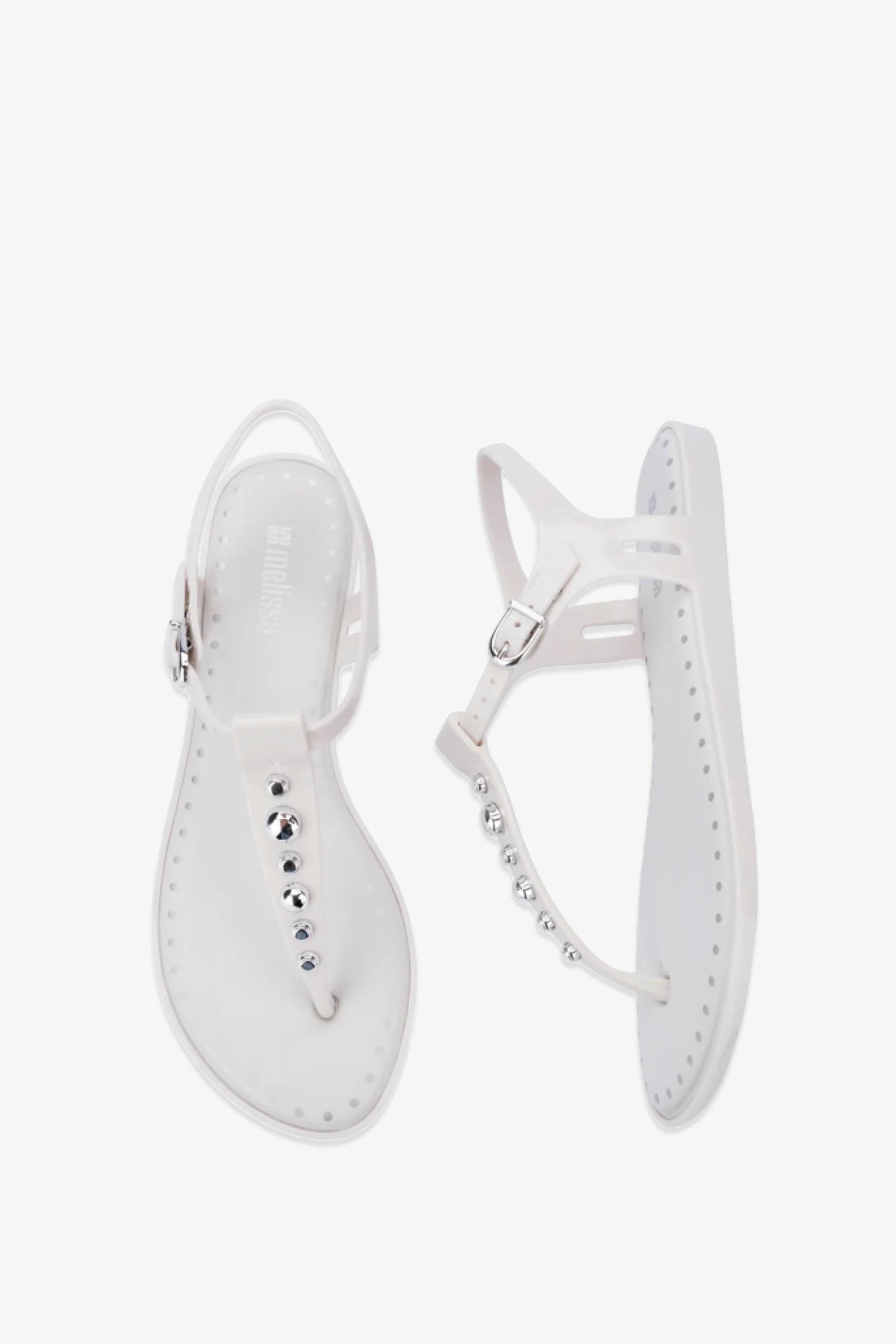 A pair of Solar Boho Thong Sandals in white featuring flat soles, ankle straps, and shiny round silver embellishments along the center strap, displayed on a white background.
