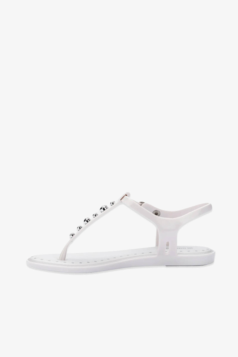The Solar Boho Thong Sandals are white flat-soled sandals featuring a T-strap design and adorned with round metallic studs along the top strap, photographed against a plain white background.
