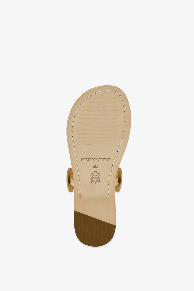 The image shows the sole of the New Moon Sandal in beige, featuring visible stitching, a small heel, gold hardware, and a sole stamped with BERNARDO and a leather quality mark.