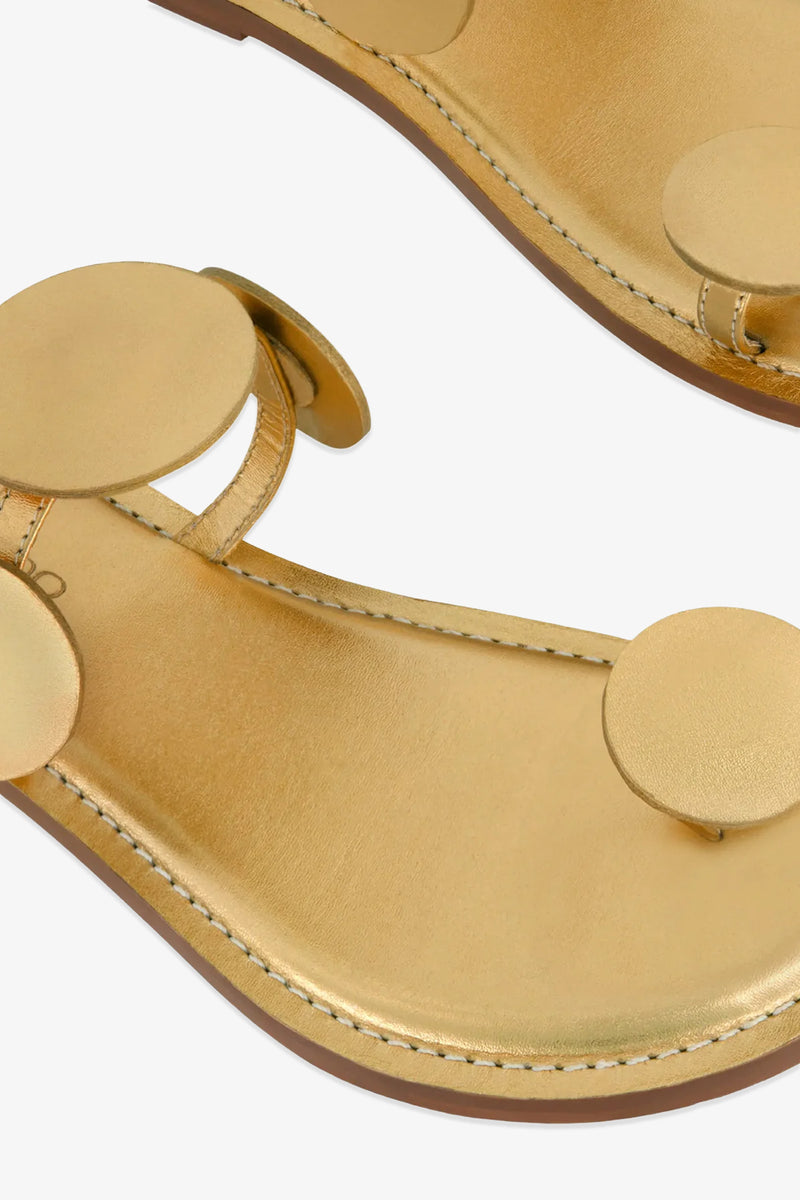 Close-up of the New Moon Sandal, featuring large round gold embellishments on the straps and footbed, visible stitching, and a smooth metallic finish.
