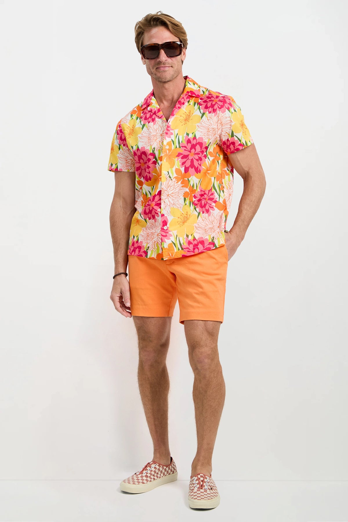 A man wearing the Felix Camp Shirt - Como, featuring bright yellow fabric with pink and red floral patterns, stands against a plain white background.