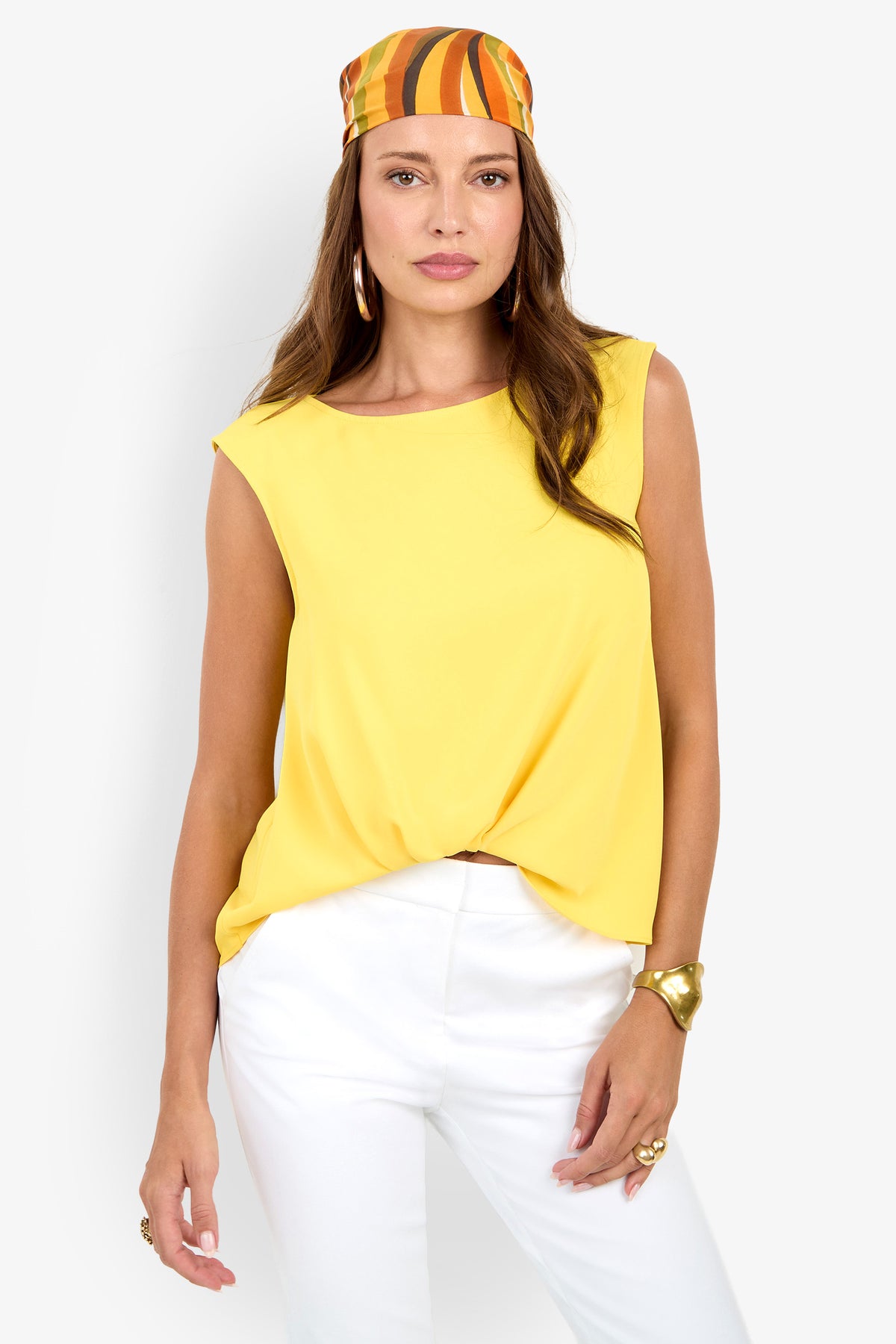 Woman wearing the Aprica Boatneck Top (Wholesale) in yellow, styled with white pants, gold bracelet, hoop earrings, and an orange-yellow patterned headscarf against a plain white background.