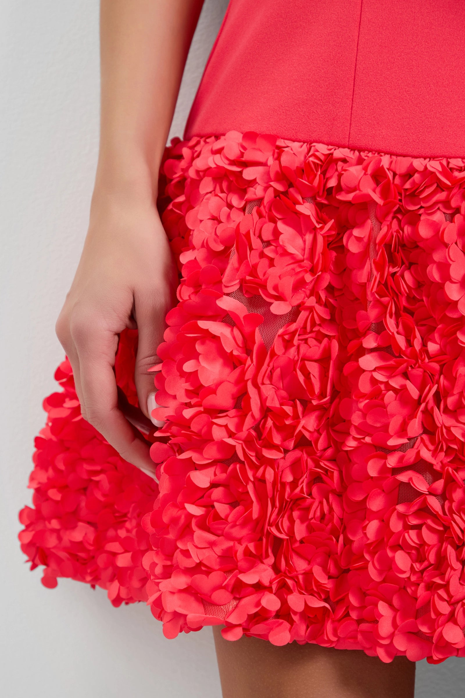 A close-up of a person wearing the Tibaldi 3D Floral Mini Dress in bright pink, featuring textured three-dimensional floral appliqués on the skirt and their left hand resting gently by their side.