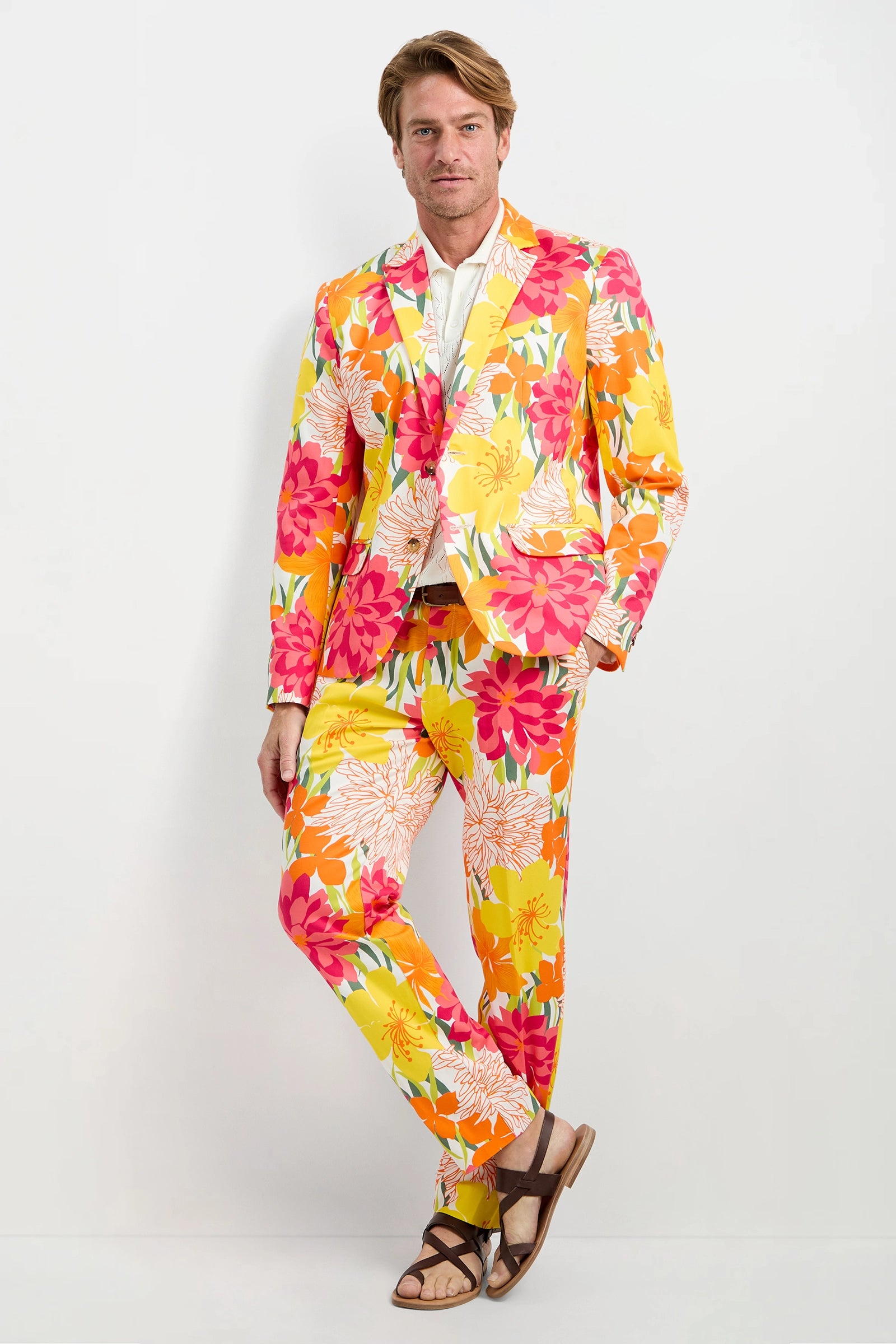 A man wearing the Clyde Slim Trouser - Como Herringbone stands against a plain white background, paired with a white shirt and brown sandals.