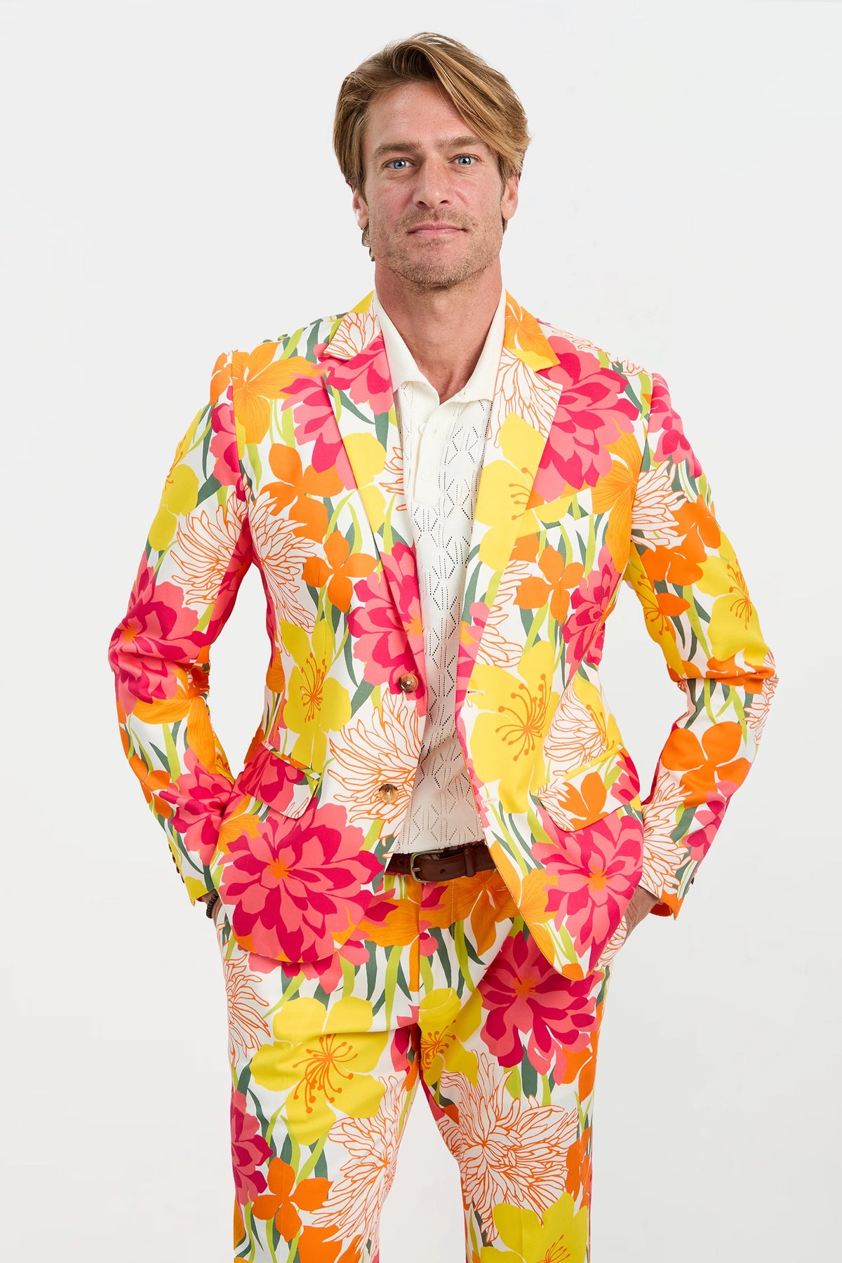 A man with blond hair and a neutral expression stands against a plain background, wearing the Thurston Blazer - Como Herringbone, his hands in his pockets.