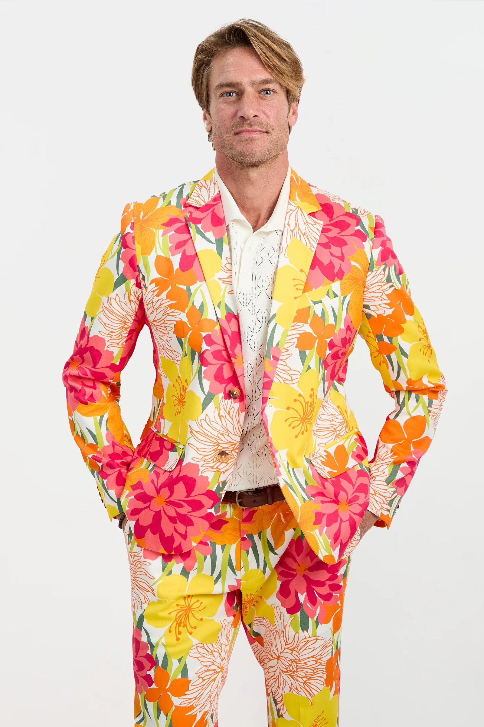 A man with blond hair and a neutral expression stands against a plain background, wearing the Thurston Blazer - Como Herringbone, his hands in his pockets.