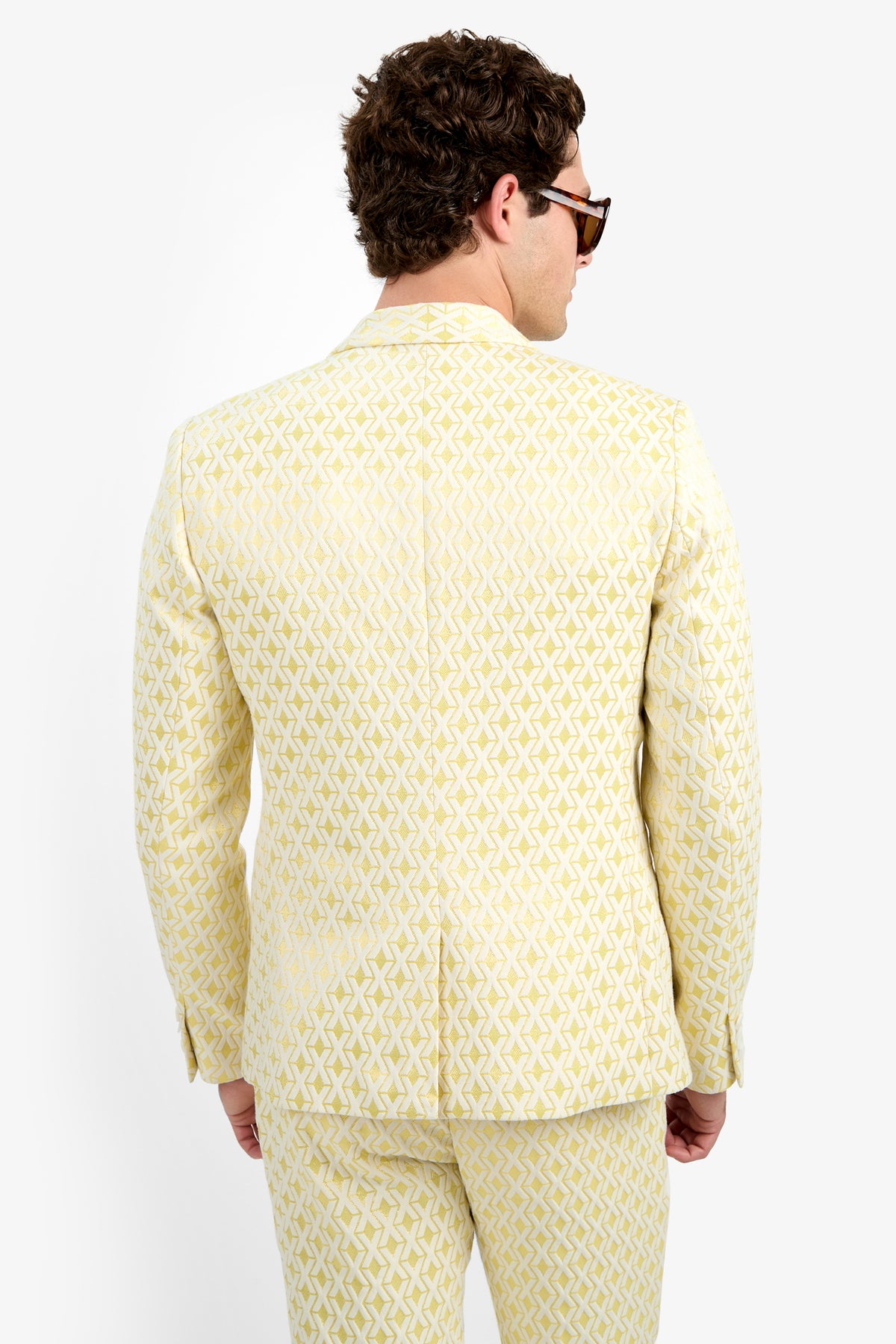 A man with curly brown hair, sunglasses, and the Thurston Blazer - Crossroads Jacquard stands with his back to the camera against a plain white background.