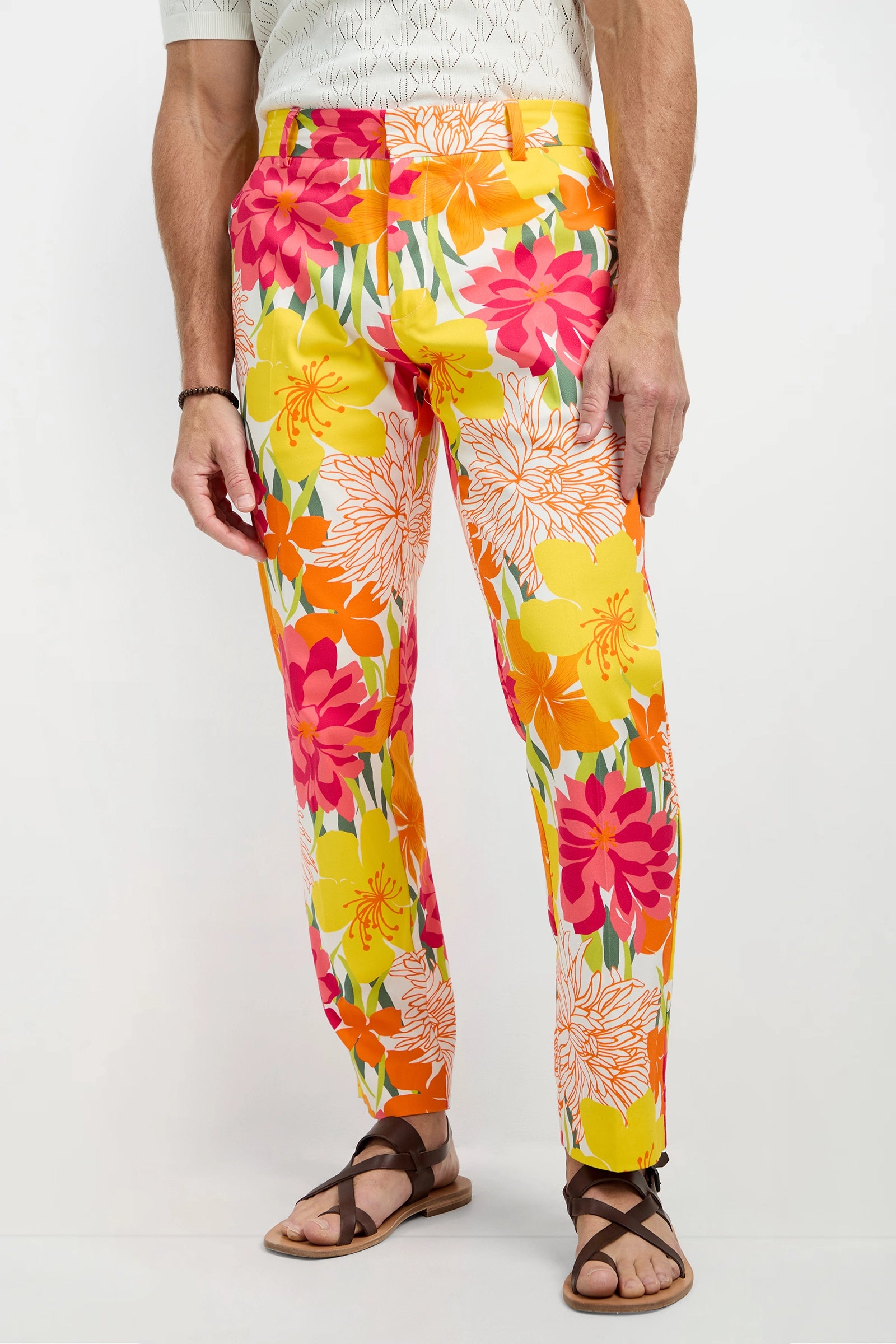 Someone wearing the Clyde Slim Trouser - Como Herringbone, a light patterned shirt, and brown sandals stands against a plain background.