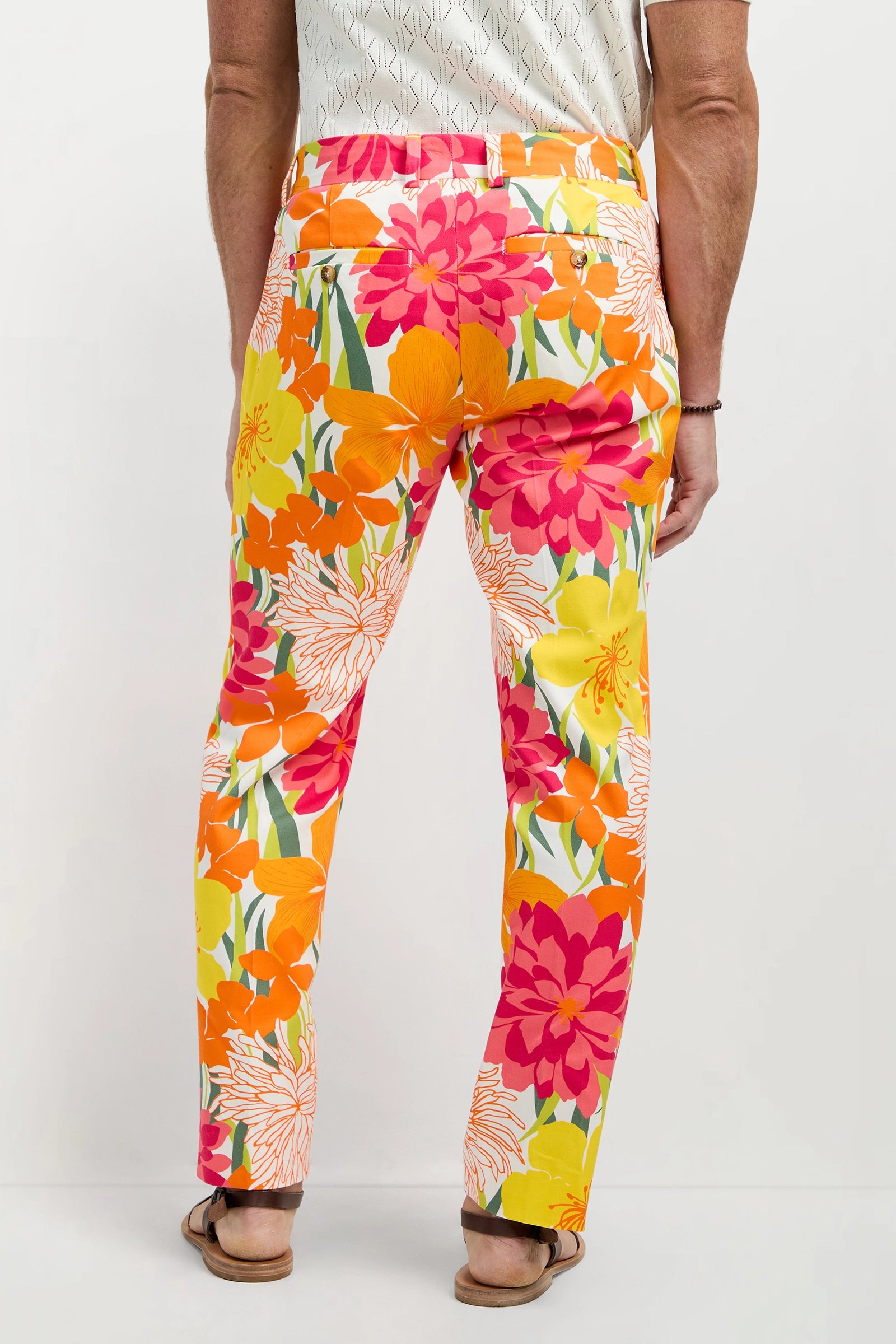 A person stands facing away, wearing the Clyde Slim Trouser - Como Herringbone paired with a light patterned shirt and sandals.