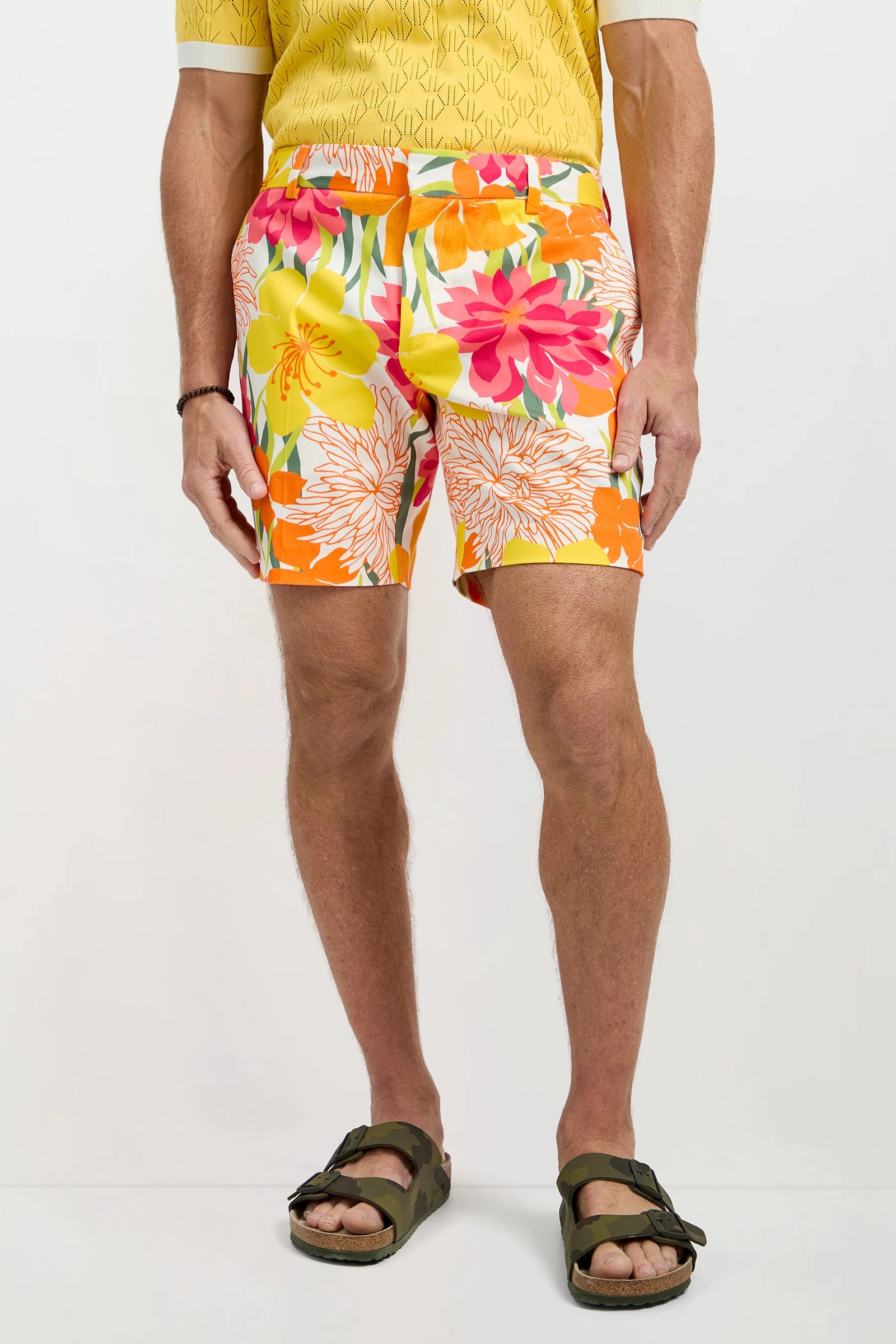 A man stands against a white background, visible from the shoulders down, wearing Lawrence Short - Como Herringbone, a yellow patterned shirt, and olive green sandals.