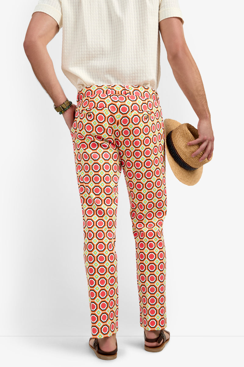 A person seen from behind wears a short-sleeve white shirt, the Clyde Slim Trouser - Salerno Herringbone, holds a straw hat, and has on sandals.