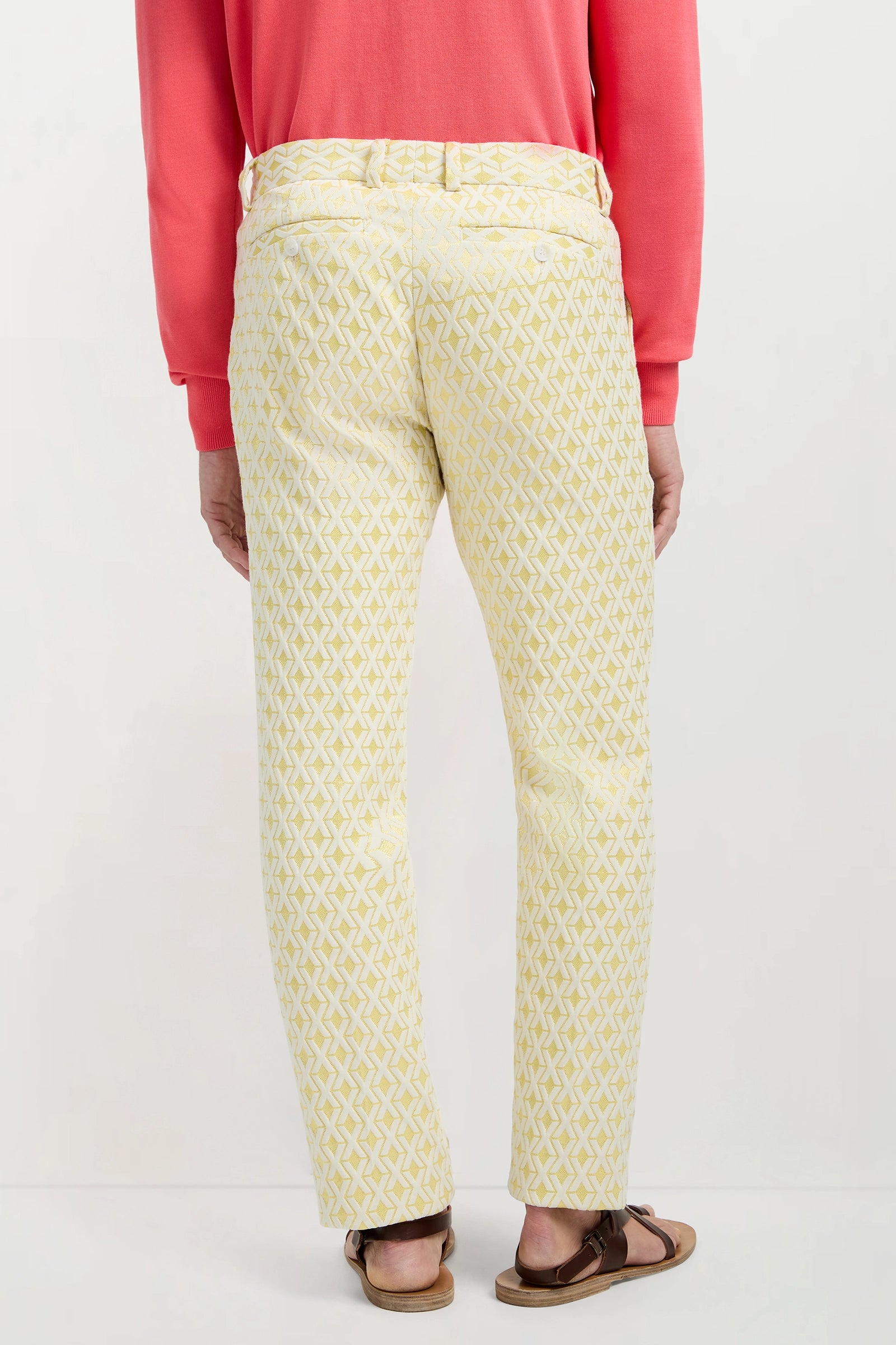 A person stands facing away against a plain white background, wearing the Clyde Slim Trouser - Crossroads Jacquard in light yellow.