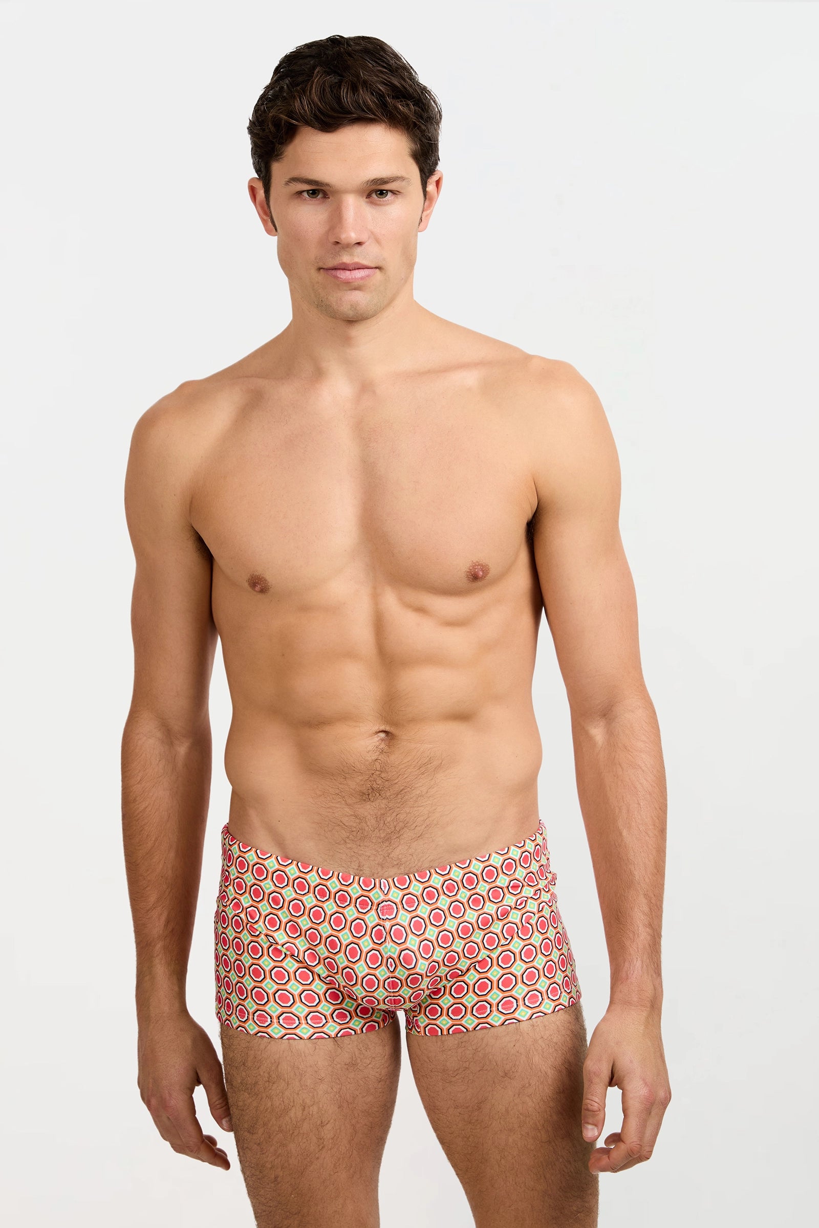 A man faces forward against a plain white background, wearing the Montego Bay Swim Trunk - Salerno featuring a colorful geometric red, yellow, and white circular pattern.