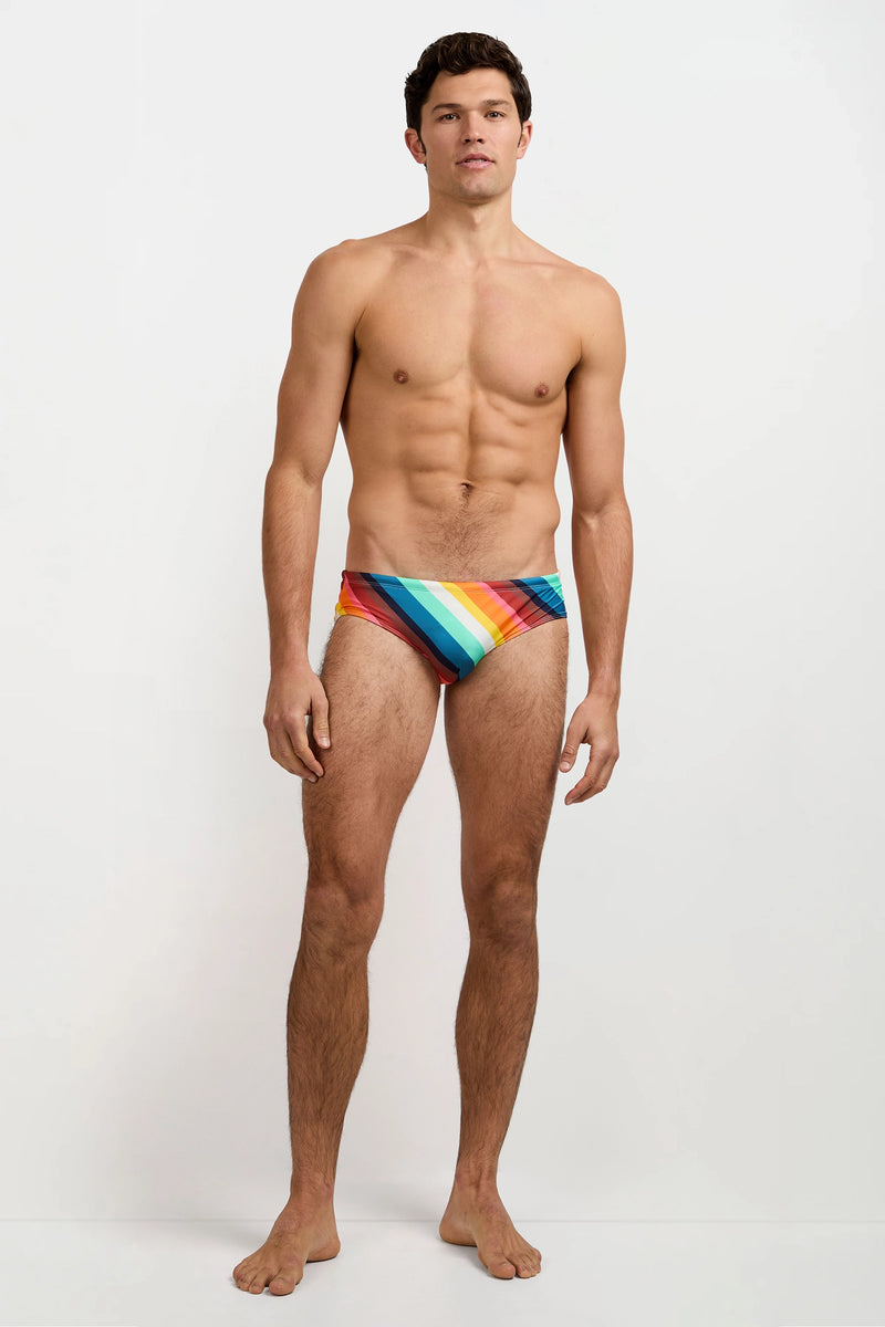 A shirtless man stands barefoot against a plain white background, facing forward with a neutral expression while wearing the Bondi Swim Brief in Siena Stripe.
