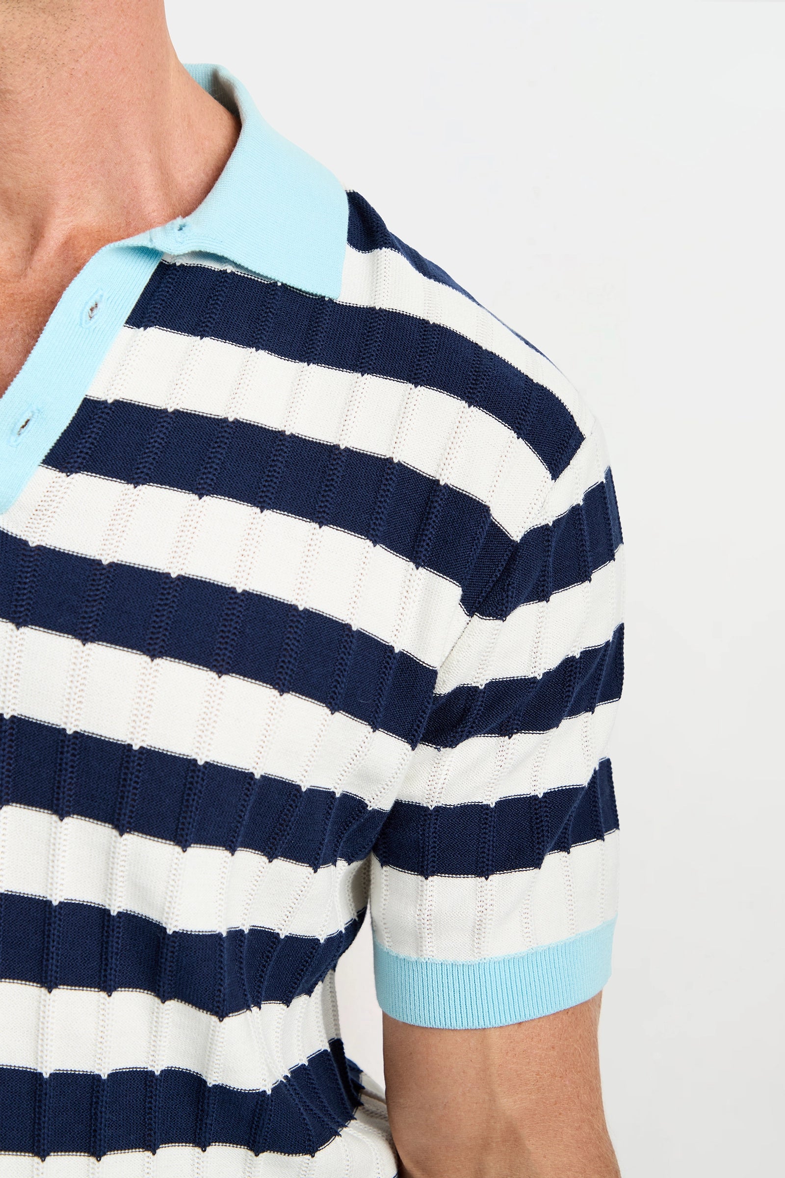 A person wears the Enzo Short-Sleeve Polo featuring blue and white stripes, a light blue collar, and sleeve cuffs. Only the upper torso and part of the left arm are visible.