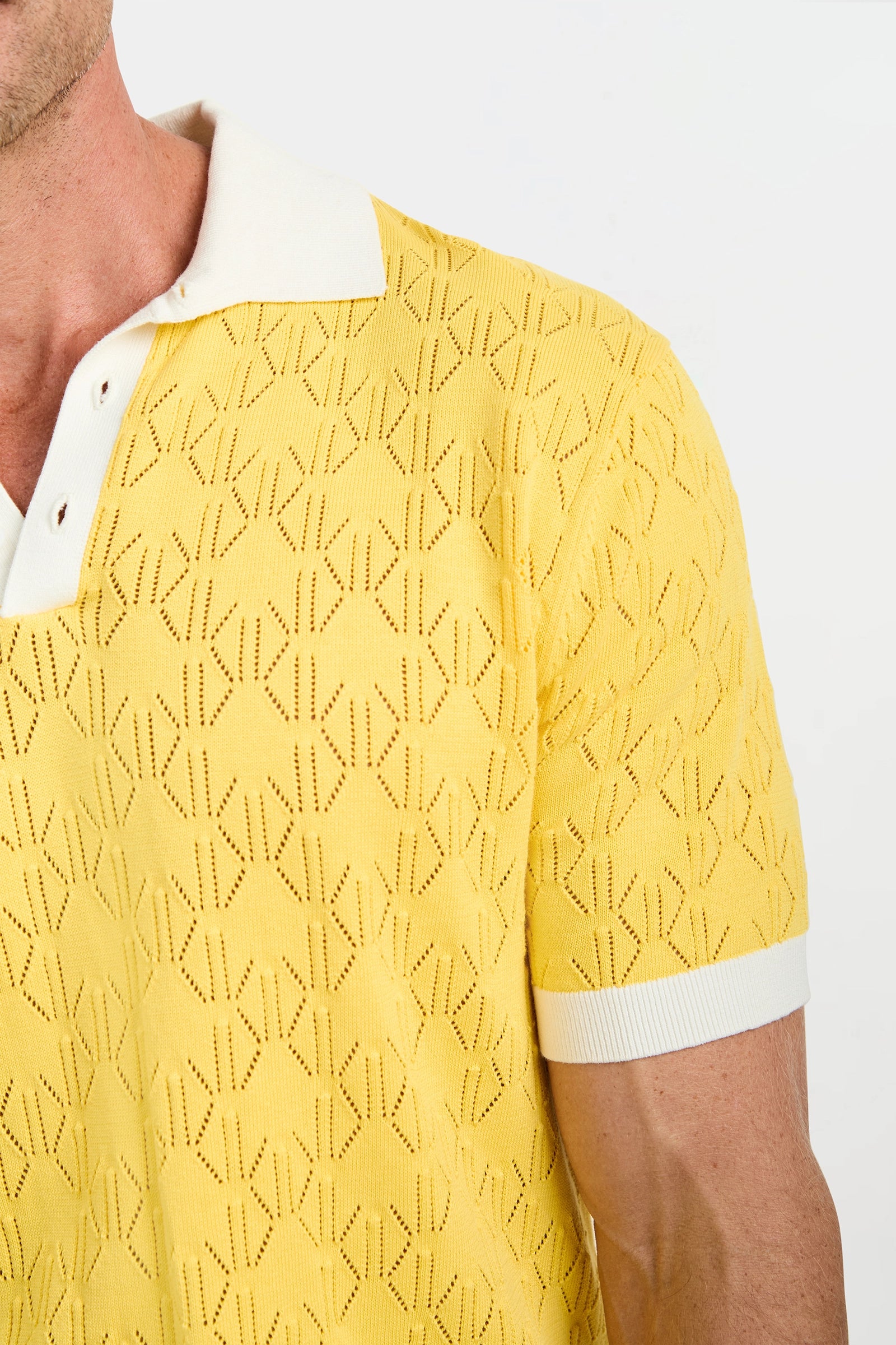 A close-up of a person wearing the Luca Short-Sleeve Polo in light yellow, featuring a geometric textured pattern, white collar, and white sleeve cuffs against a plain background.