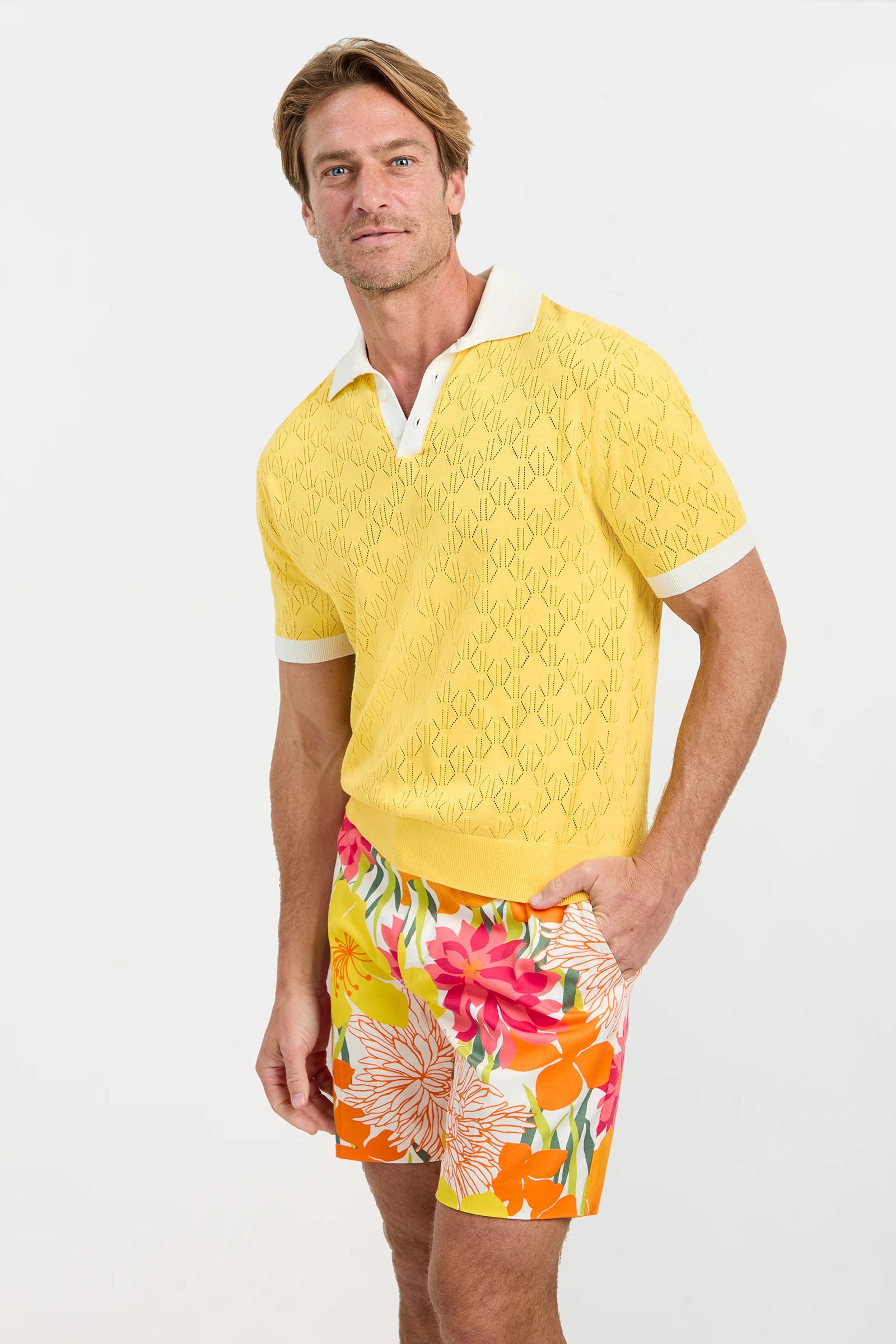 Man wearing a yellow textured shirt and colorful floral shorts on a white background