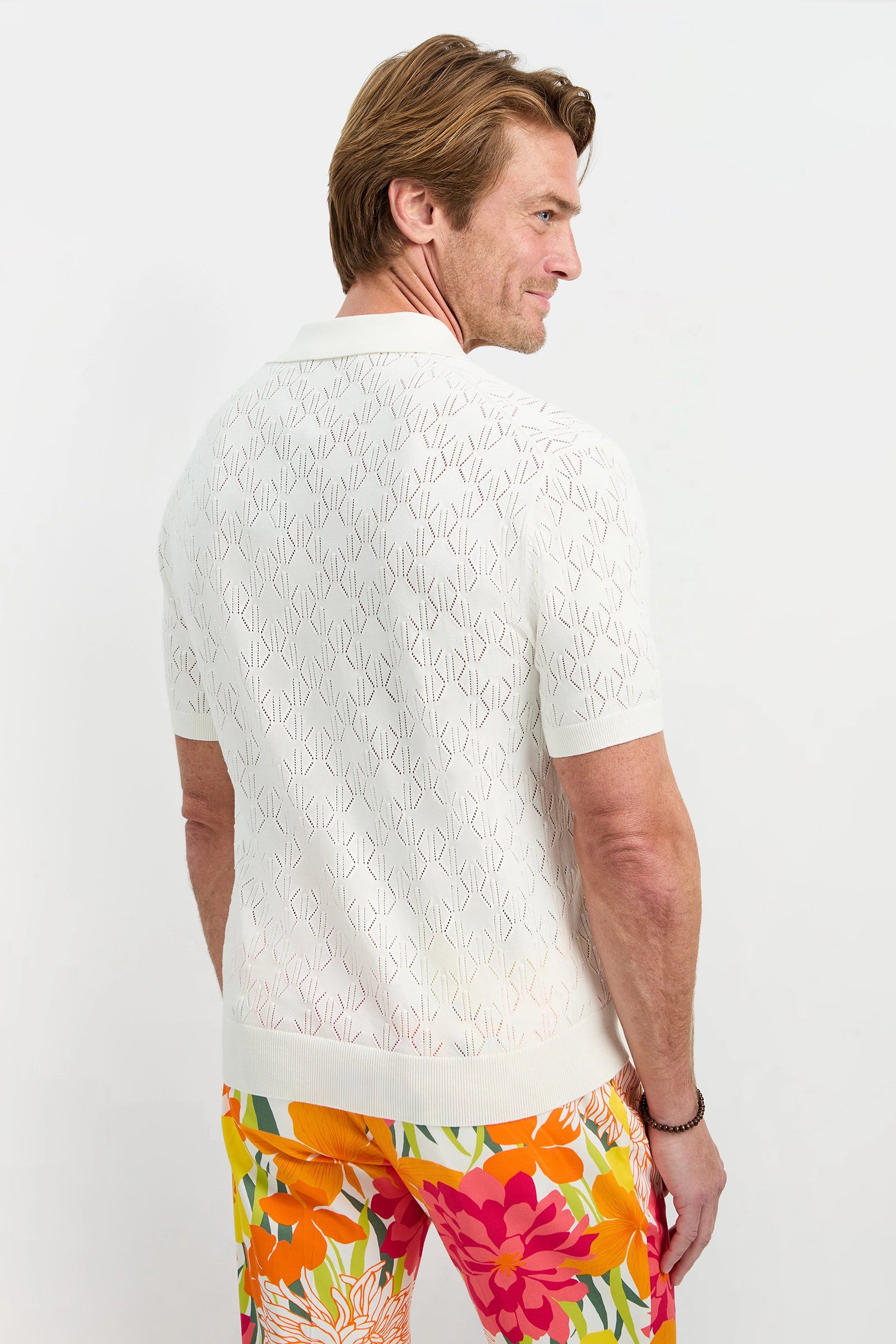 A man faces away, wearing the Luca Short-Sleeve Polo and bright floral pants with orange, pink, and yellow flowers, set against a plain white background.