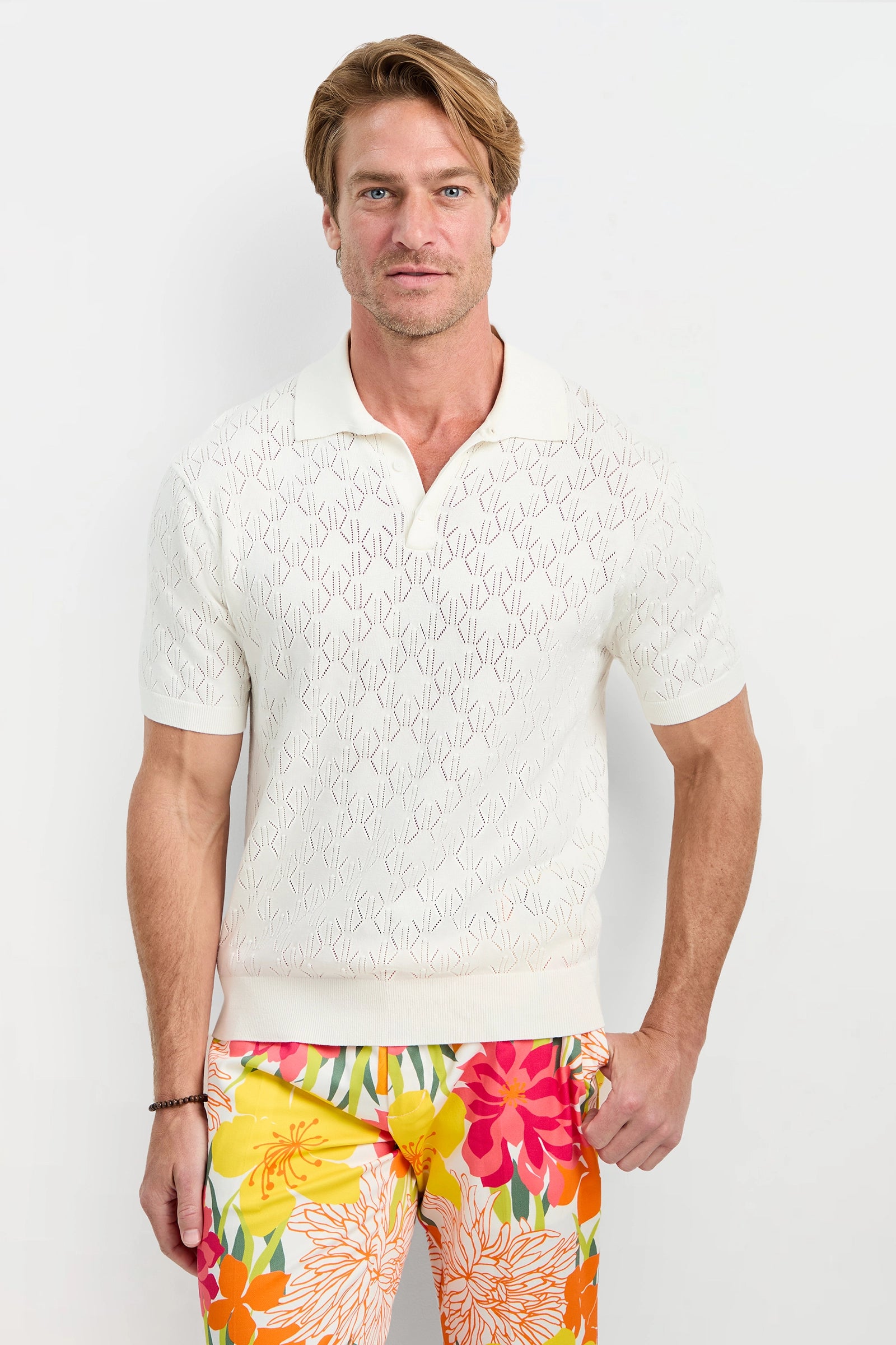 Man wearing a white textured shirt and colorful floral pants on a white background