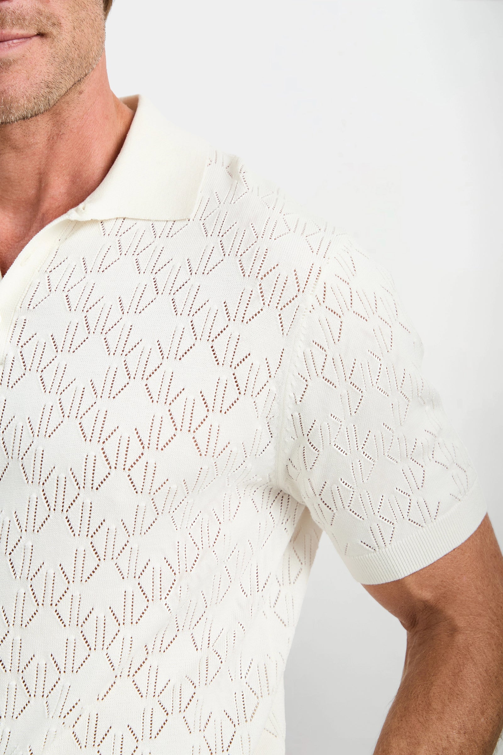 Man wearing a white polo shirt with a subtle pattern on a plain background