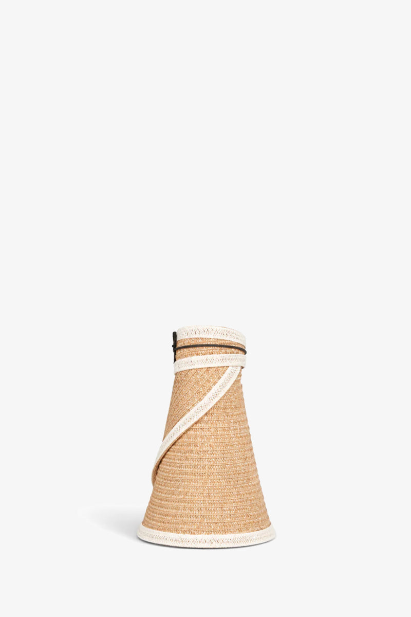 The Trixie Visor is a woven, cone-shaped straw bag featuring white trim and a slim tan shoulder strap, shown on a plain white background.