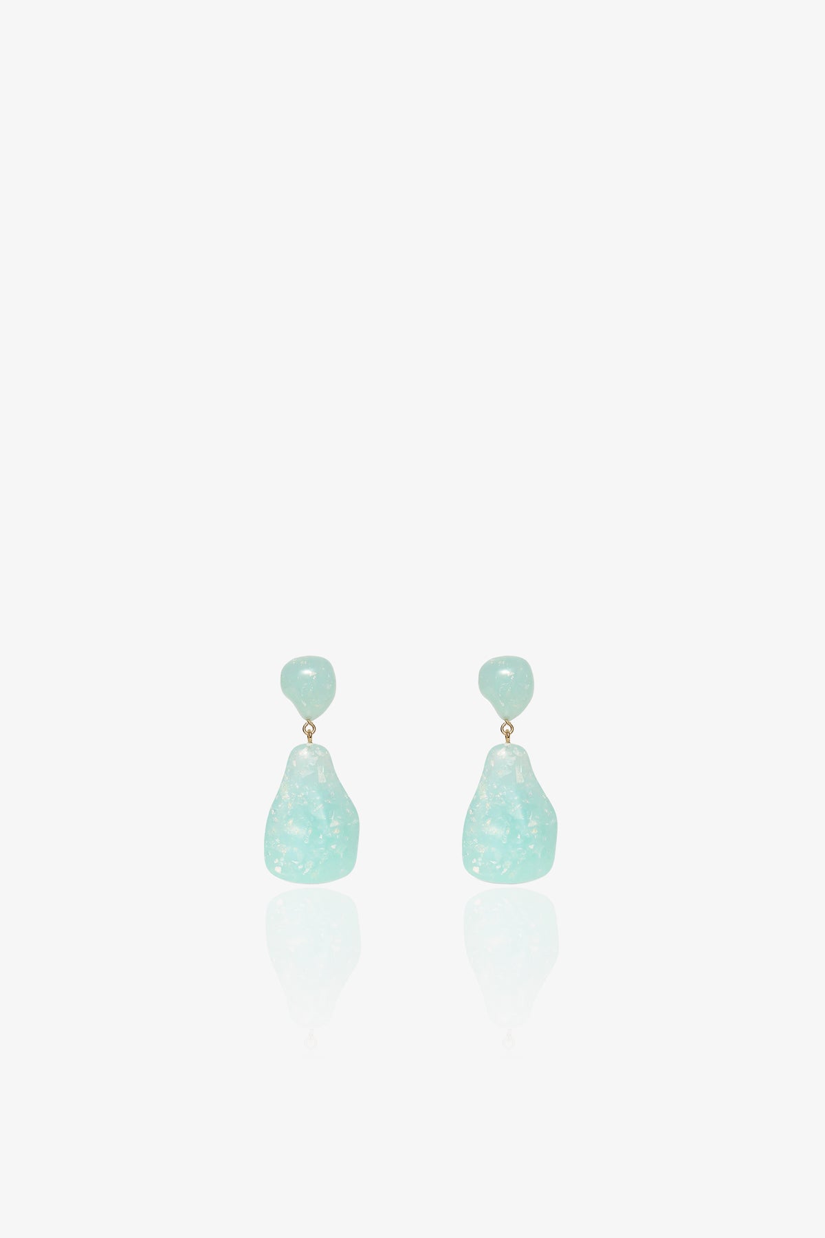 The Wilma Earrings feature small, round, light blue studs and larger, irregularly shaped translucent blue drops in a dangling design, displayed against a white background.