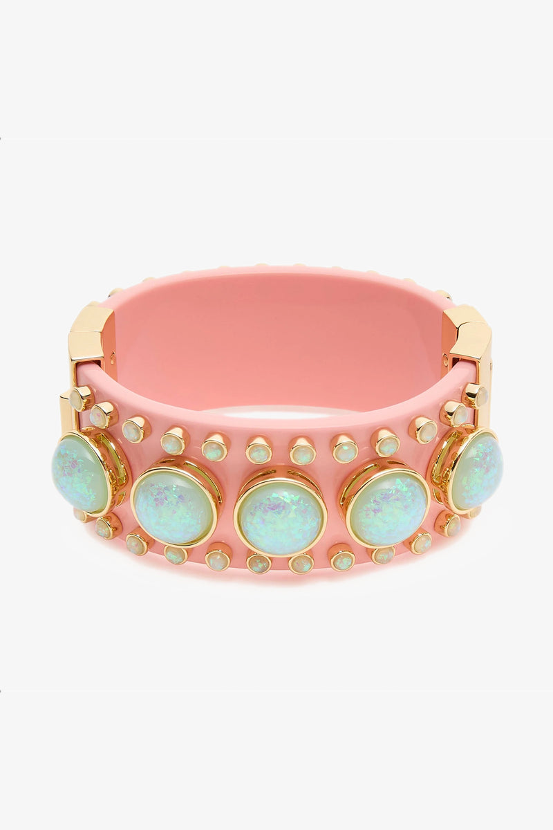 The Deco Hinged Cuff is a wide pink bracelet with gold accents, adorned with large iridescent opal-like stones and rows of small round studs around its surface.