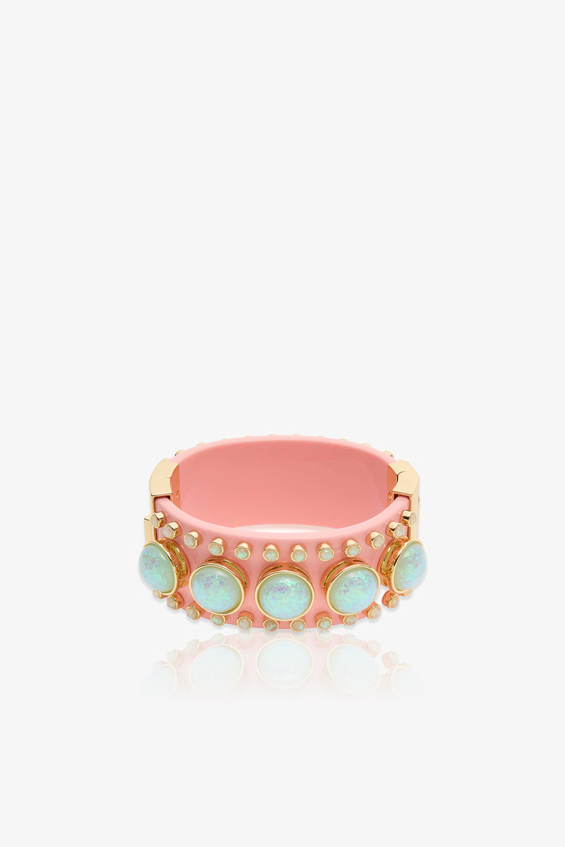 The Deco Hinged Cuff is a pink bracelet with gold edges, featuring five round opal-like stones set in gold bezels, each accented by small gold studs.