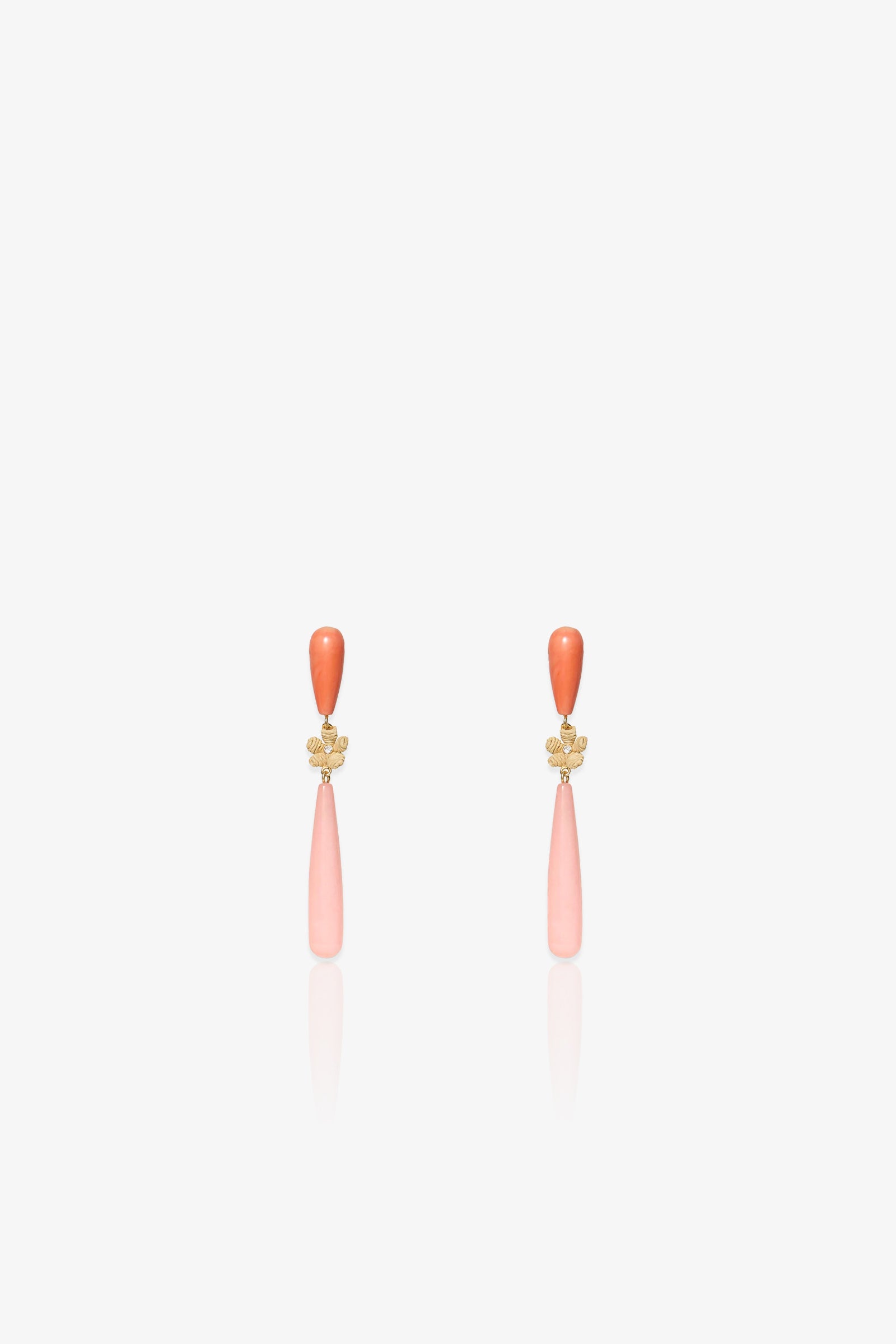 The Flamingo Linear Earring is an elegant pair of drop earrings featuring a small orange bead at the top, a gold floral accent in the middle, and a long, light pink teardrop-shaped pendant hanging below, displayed on a white background.
