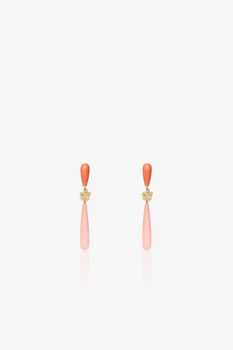 The Flamingo Linear Earring is an elegant pair of drop earrings featuring a small orange bead at the top, a gold floral accent in the middle, and a long, light pink teardrop-shaped pendant hanging below, displayed on a white background.