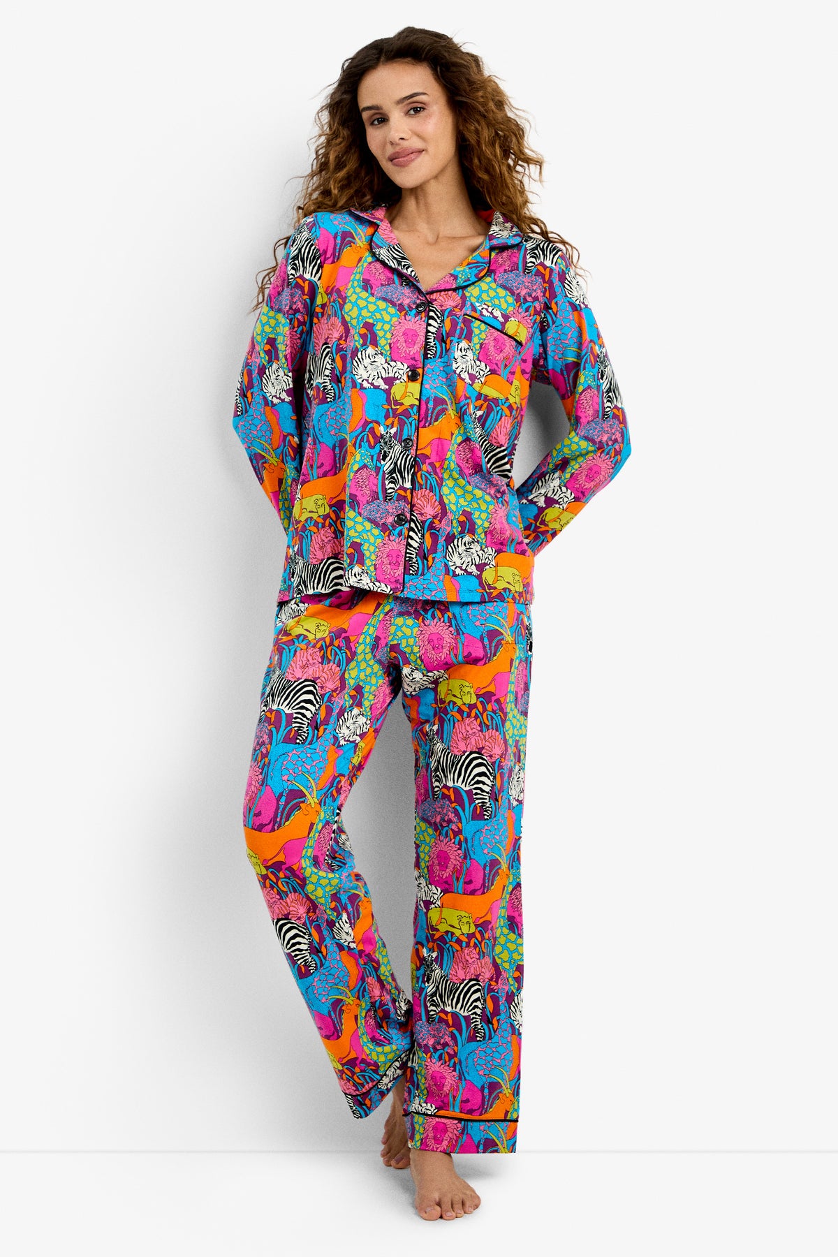 A woman stands barefoot wearing the Classic PJ Set - Jungle, featuring a vibrant jungle-themed pattern with wild animals on a white background.