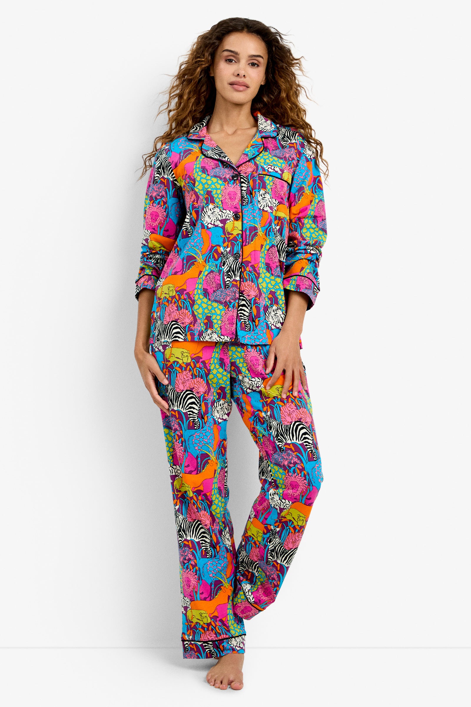 A person stands barefoot in the Classic PJ Set - Jungle, featuring colorful animal prints like zebras and giraffes with vibrant floral designs, set against a plain white background.