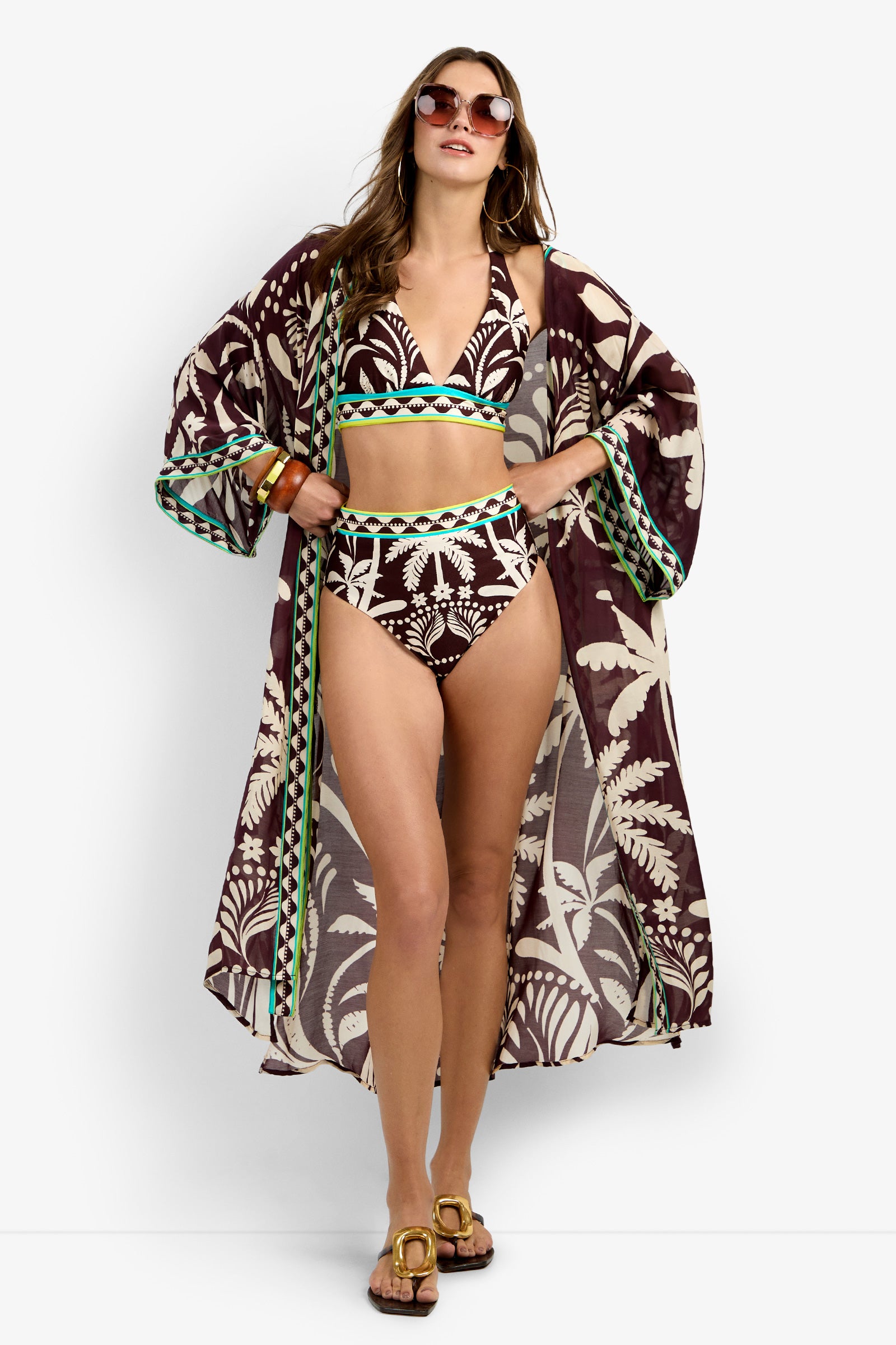 A woman confidently wears sunglasses, bangles, sandals, a brown and white patterned bikini, and the Kimono Maxi Duster in Multi.