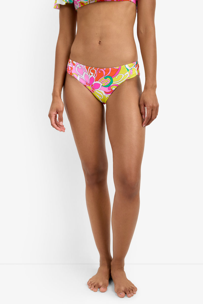 A woman stands barefoot against a white background, wearing Shirred Hipster Swim Bottoms with a colorful floral pattern and a matching bikini top partially visible. Her arms rest relaxed at her sides.