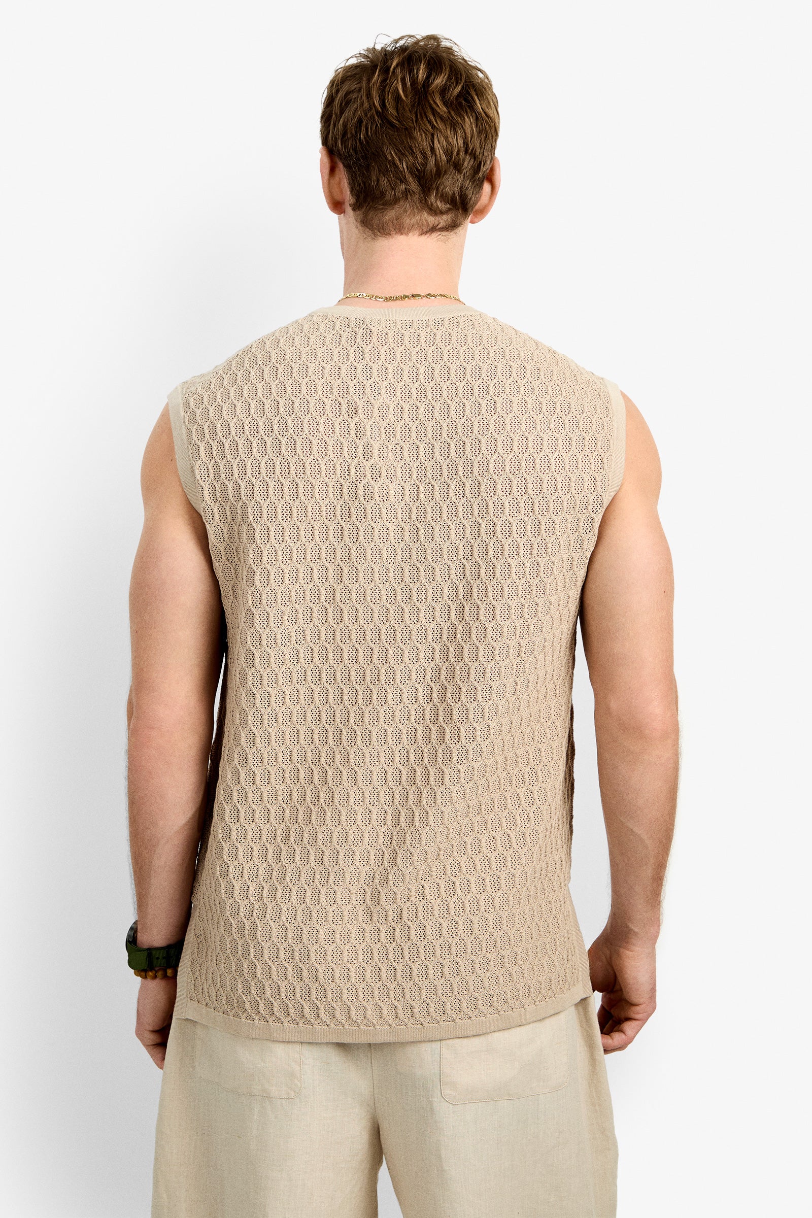 A man, seen from behind, wears the Tovey Mesh Tan sleeveless knit top and light-colored shorts while standing against a plain white background.