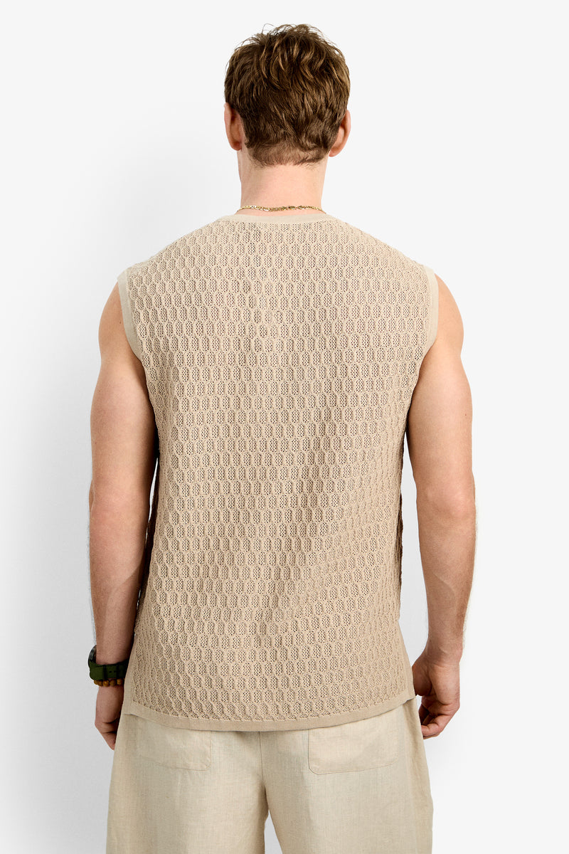 A man, seen from behind, wears the Tovey Mesh Tan sleeveless knit top and light-colored shorts while standing against a plain white background.