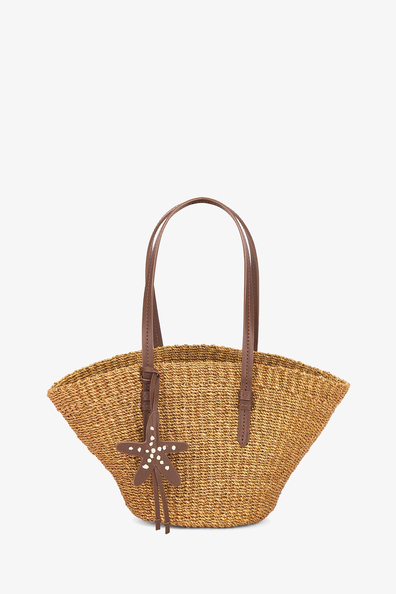 The East West Mini Tote in Cocoa features woven straw, brown leather handles, and a starfish-shaped leather charm with studs, shown against a white background.