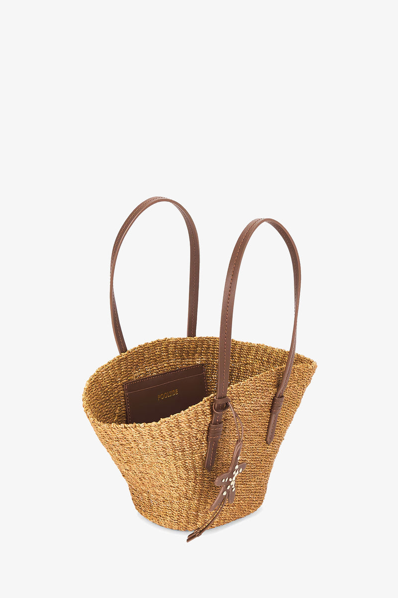 The East West Mini Tote is a medium woven straw bag with two brown leather handles, a leather tag, and an interior pocket, shown against a plain white background.