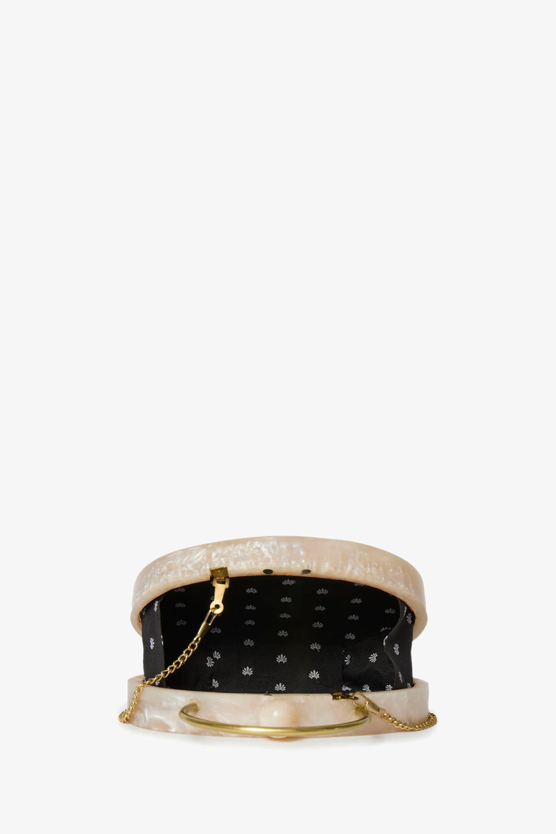 The Ivory Pearl Oval Minaudiere features a pearly beige exterior, gold chain strap, and black fabric lining with white floral pattern. Its open oval shape is shown against a plain white background.