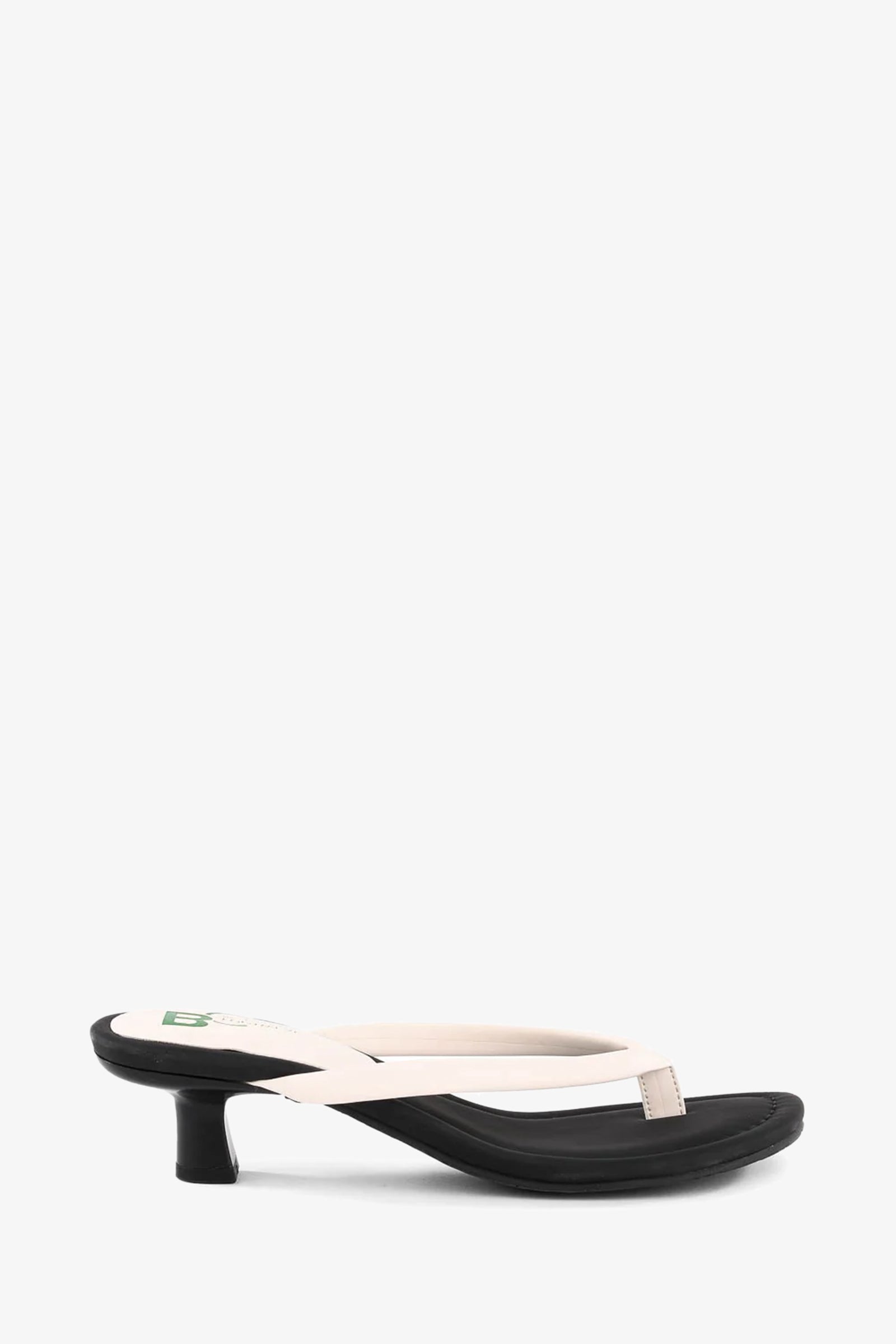 Riptide Sandal: cream leather thong sandal featuring a black kitten heel and black footbed, shown in side view on a white background.