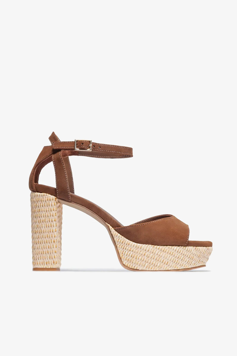 The Valeria Platform Sandal is a brown suede high-heeled shoe with an ankle strap and buckle, featuring a thick woven platform and block heel.