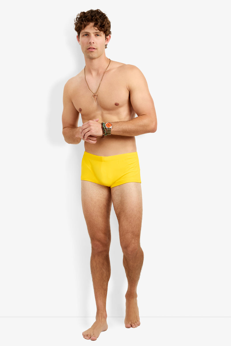 A shirtless man wearing Montego Bay Swim Trunk, bracelets, and a necklace stands barefoot against a plain white background.