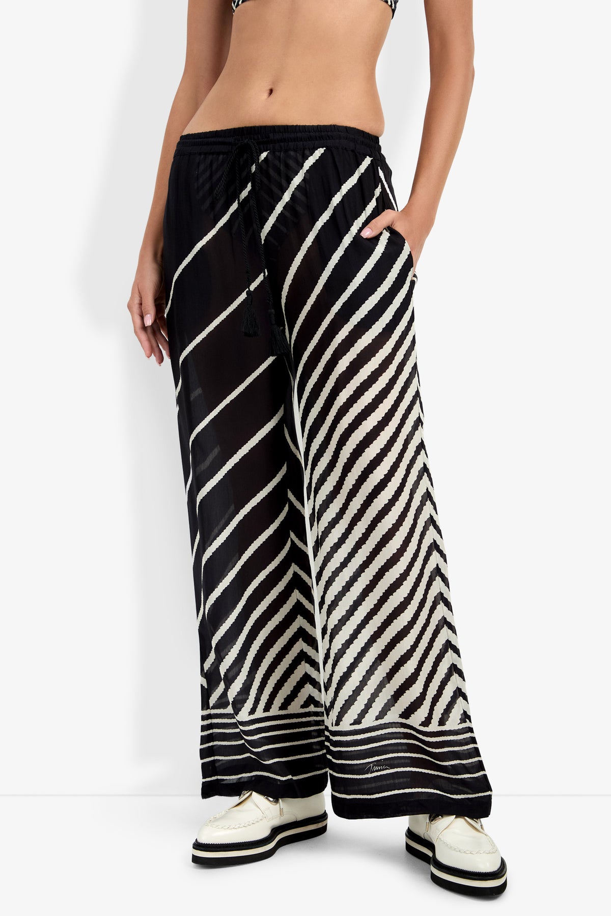 A person wearing Net Stripe Beach Pant featuring black and white diagonal and horizontal stripes, paired with white platform shoes; only the lower half of the body is shown.