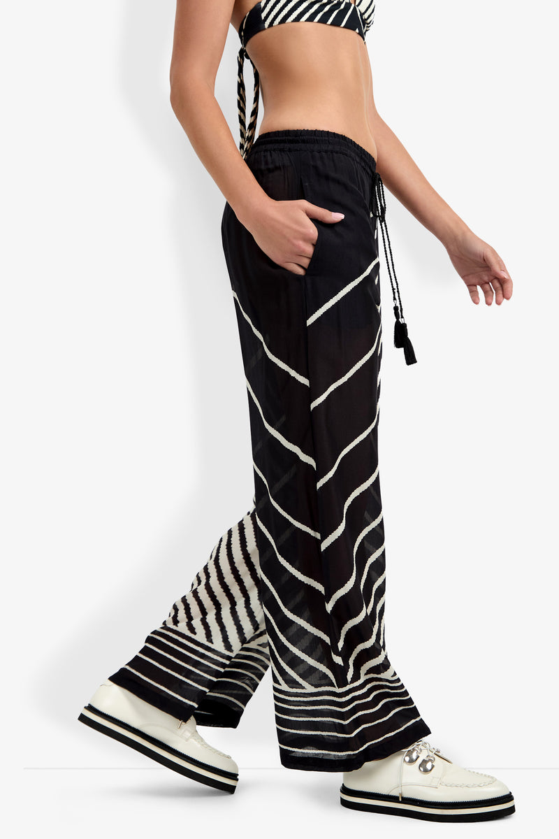 A person wearing the Net Stripe Beach Pant with a matching striped bikini top and white platform shoes walks to the right against a plain background.