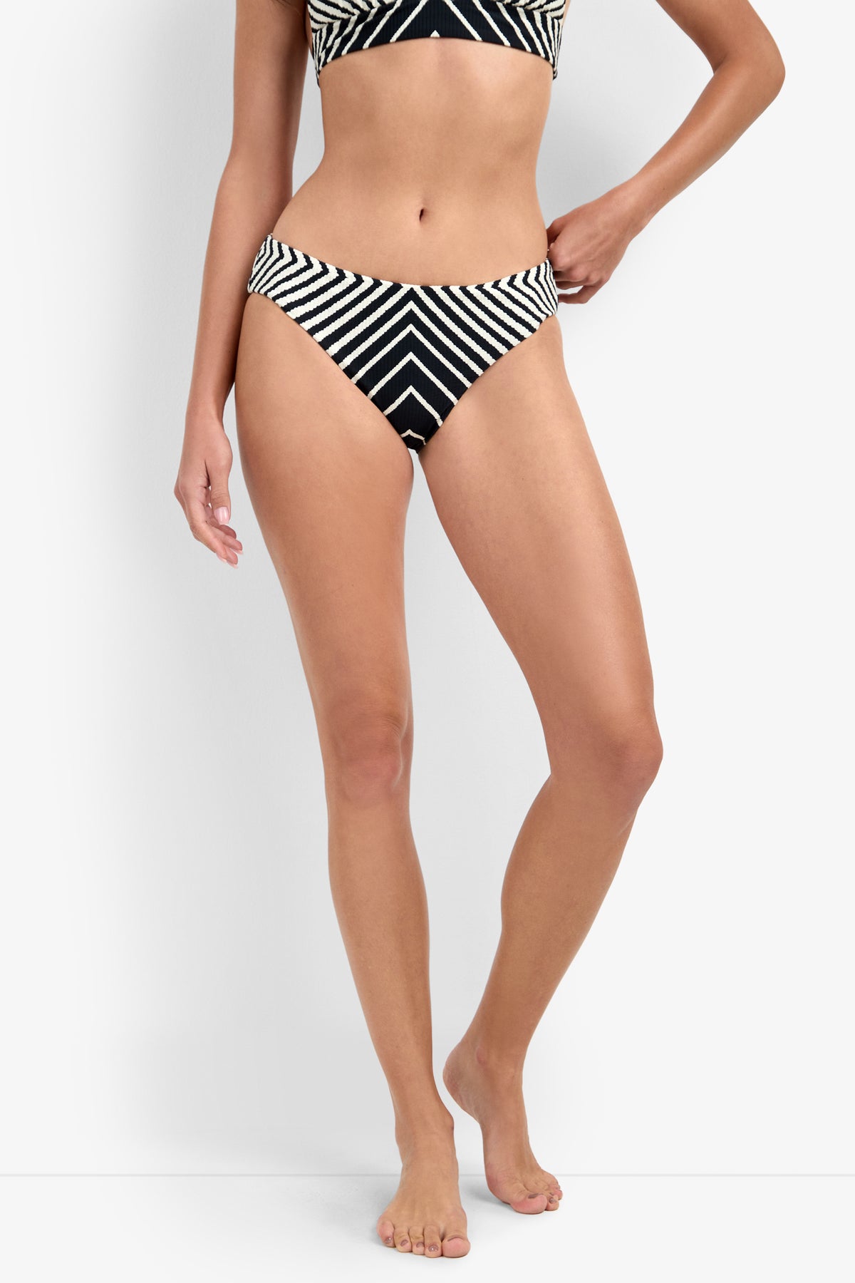 A person wears the Net Stripe Hipster Bikini Bottom, featuring black and white diagonal and chevron stripes, against a white background; only the lower torso and legs are visible.