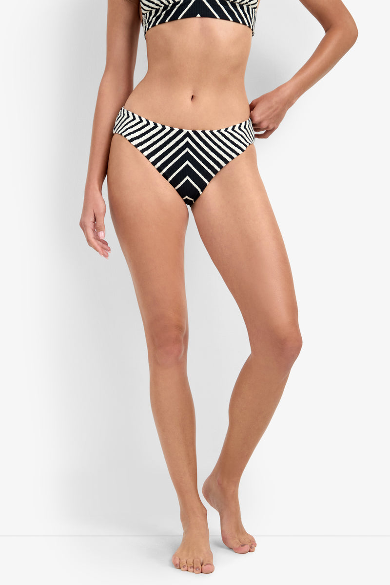 A person wears the Net Stripe Hipster Bikini Bottom, featuring black and white diagonal and chevron stripes, against a white background; only the lower torso and legs are visible.