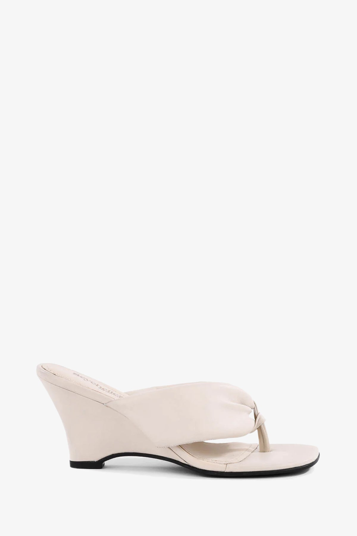 The Wishing Well Wedge: a single cream-colored sandal featuring an open toe, thong strap, and low angled wedge heel, displayed against a plain white background.