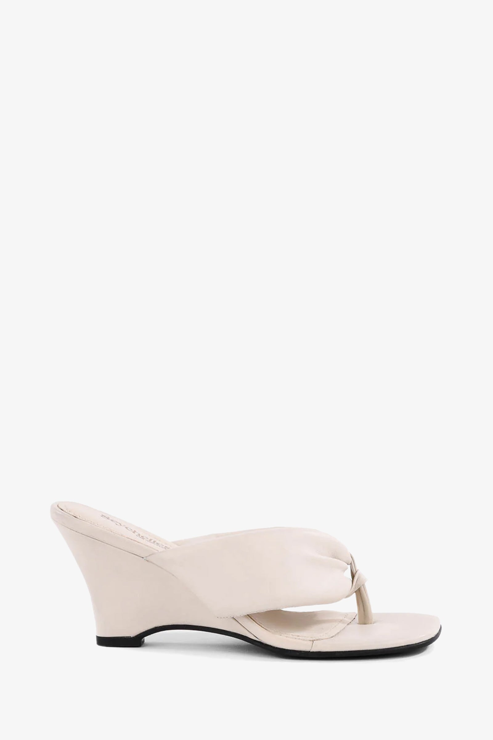 The Wishing Well Wedge: a single cream-colored sandal featuring an open toe, thong strap, and low angled wedge heel, displayed against a plain white background.