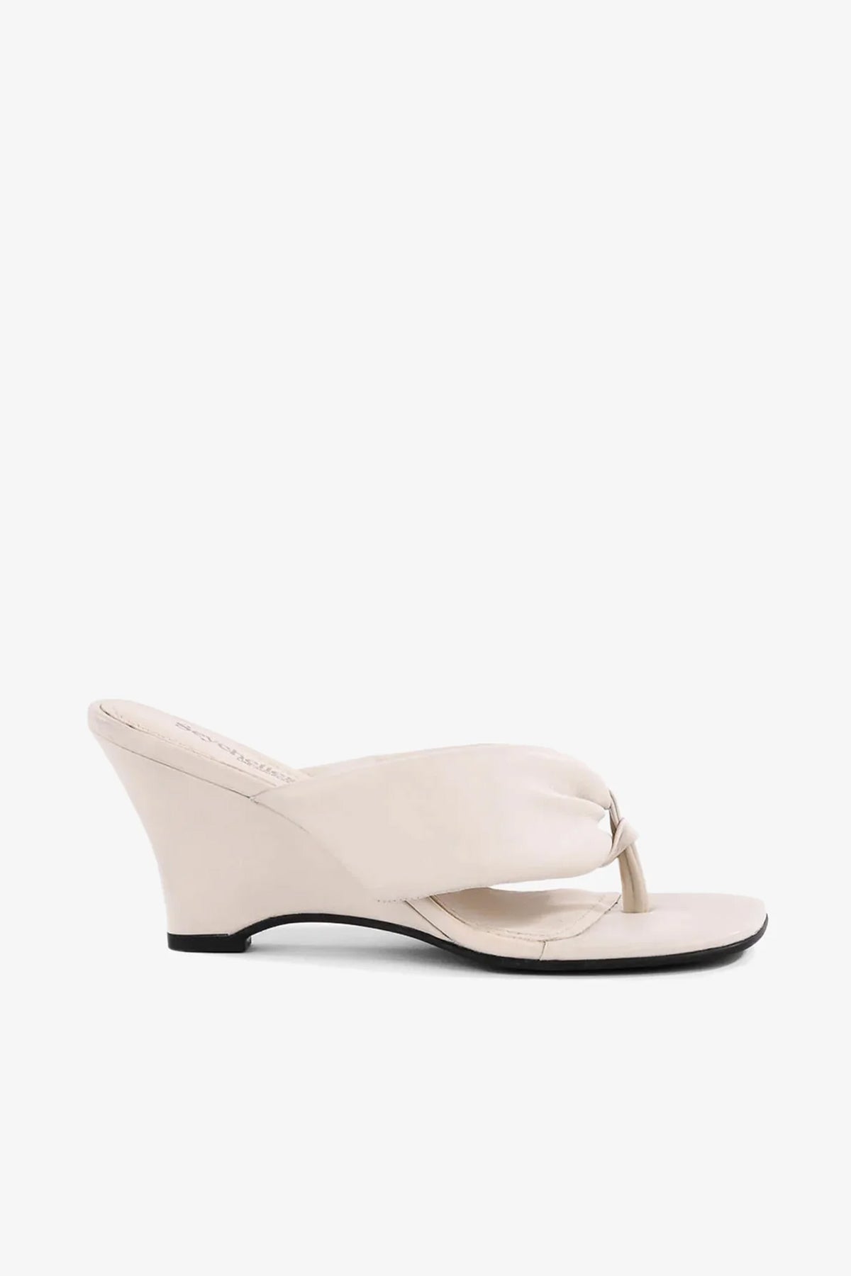The Wishing Well Wedge is a beige sandal featuring a thong toe strap, wedge heel, and smooth, minimalist design, displayed in side profile against a plain white background.